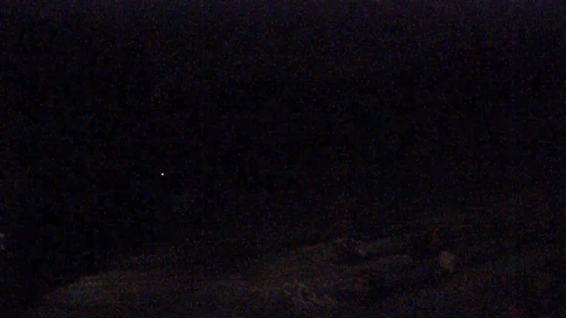 A dark, nighttime scene shows a faint light in the distance.