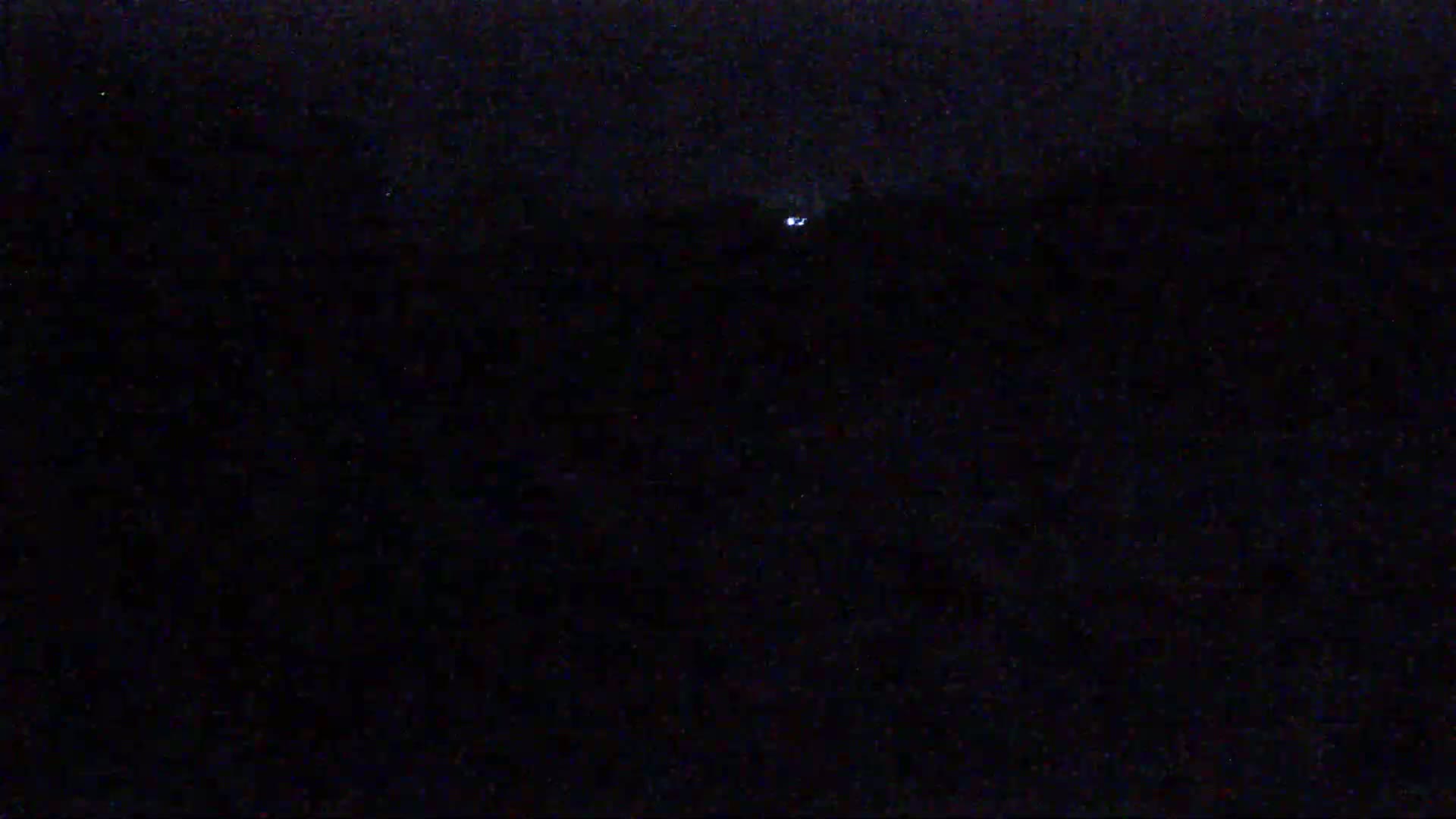 A dimly lit, dark scene at night shows a single, small light source in the distance.