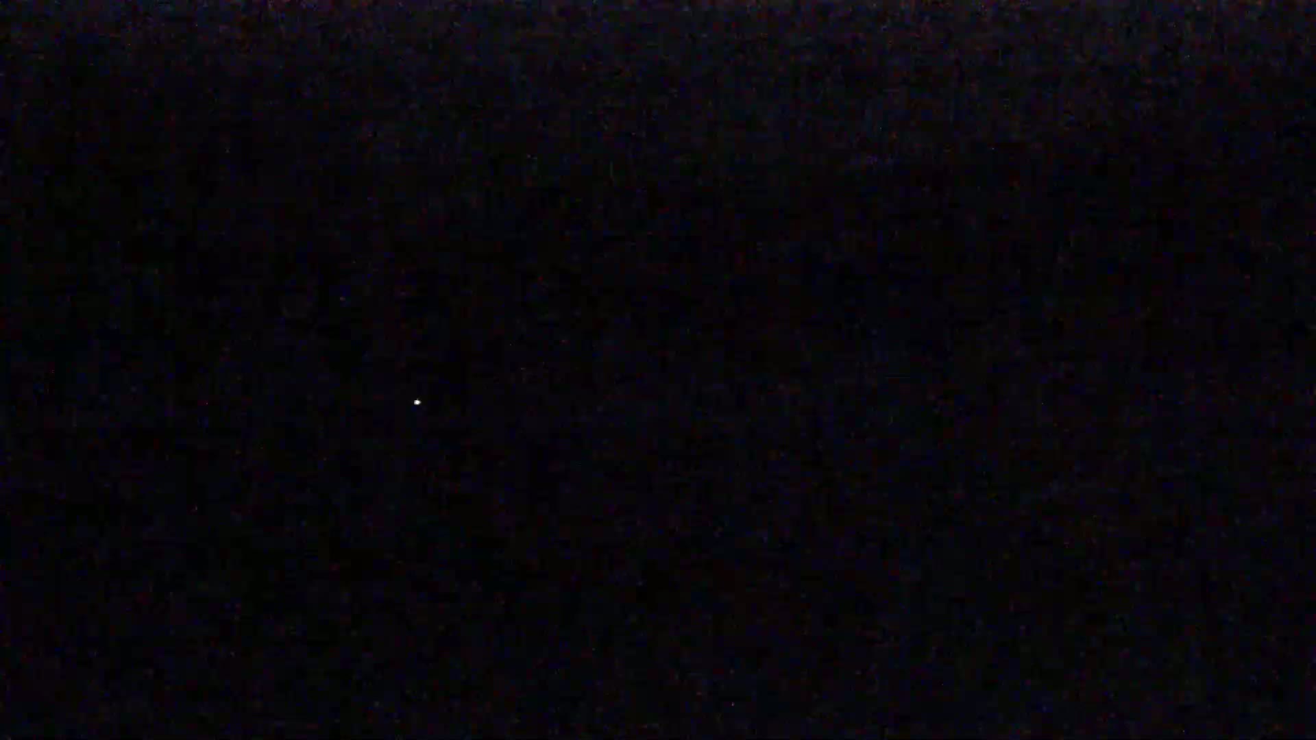 A single, faint light is visible in a dark, nighttime sky.