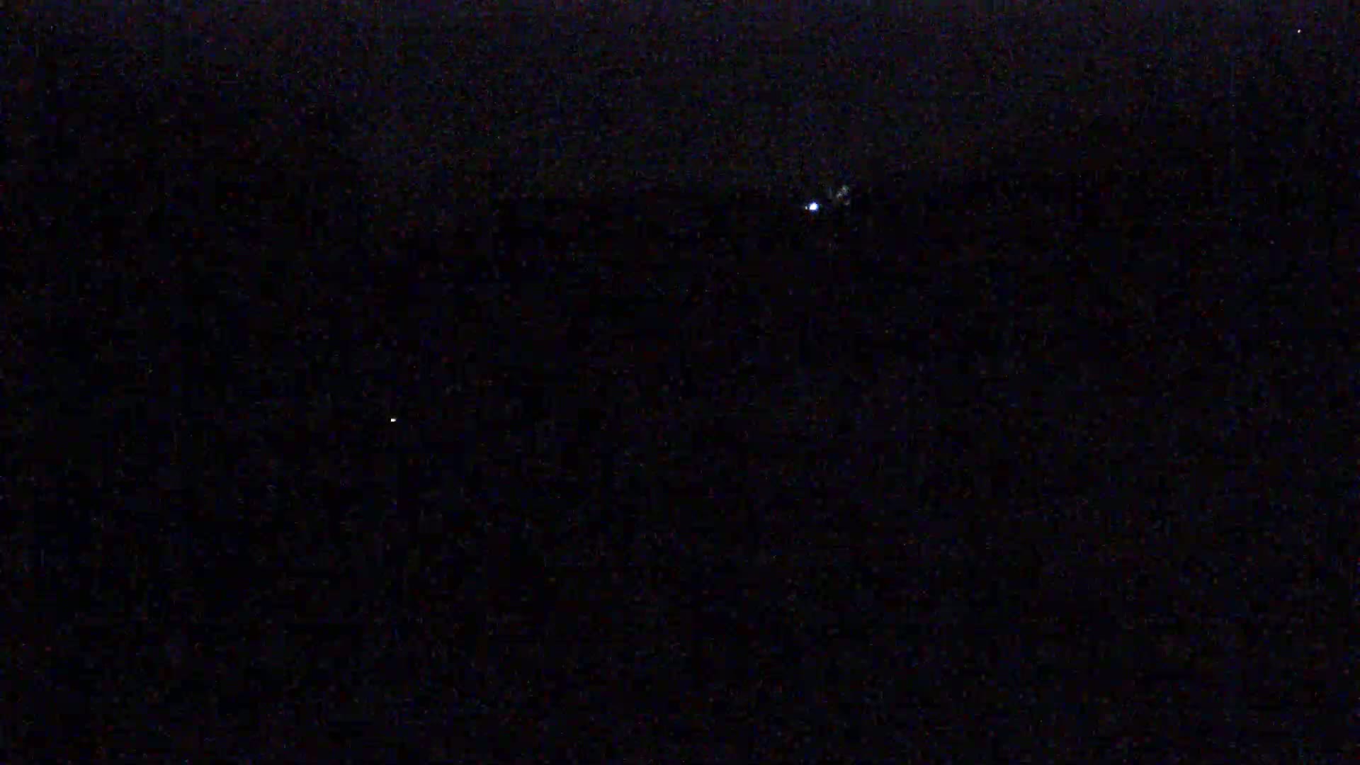 The image shows a dark, nighttime scene with a few faint lights visible in the distance.