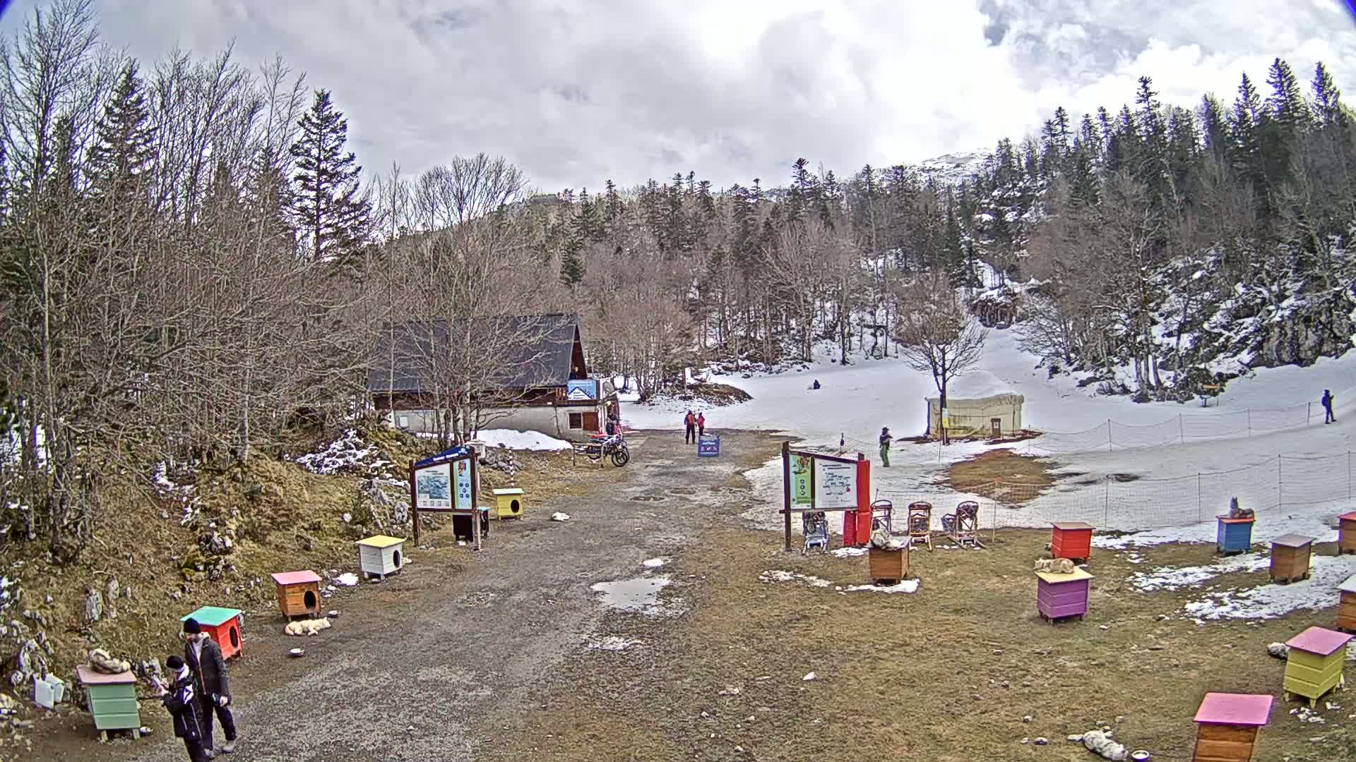 A small, snowy ski area with a few people, a building, and colorful dog houses sits under a cloudy sky.