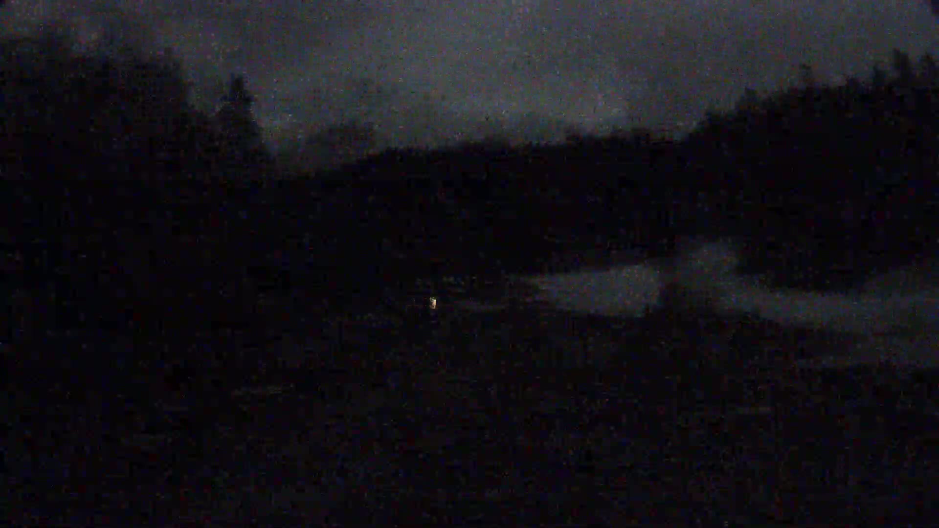 A dark, nighttime scene shows a body of water reflecting a dim sky and silhouetted trees along the shore.