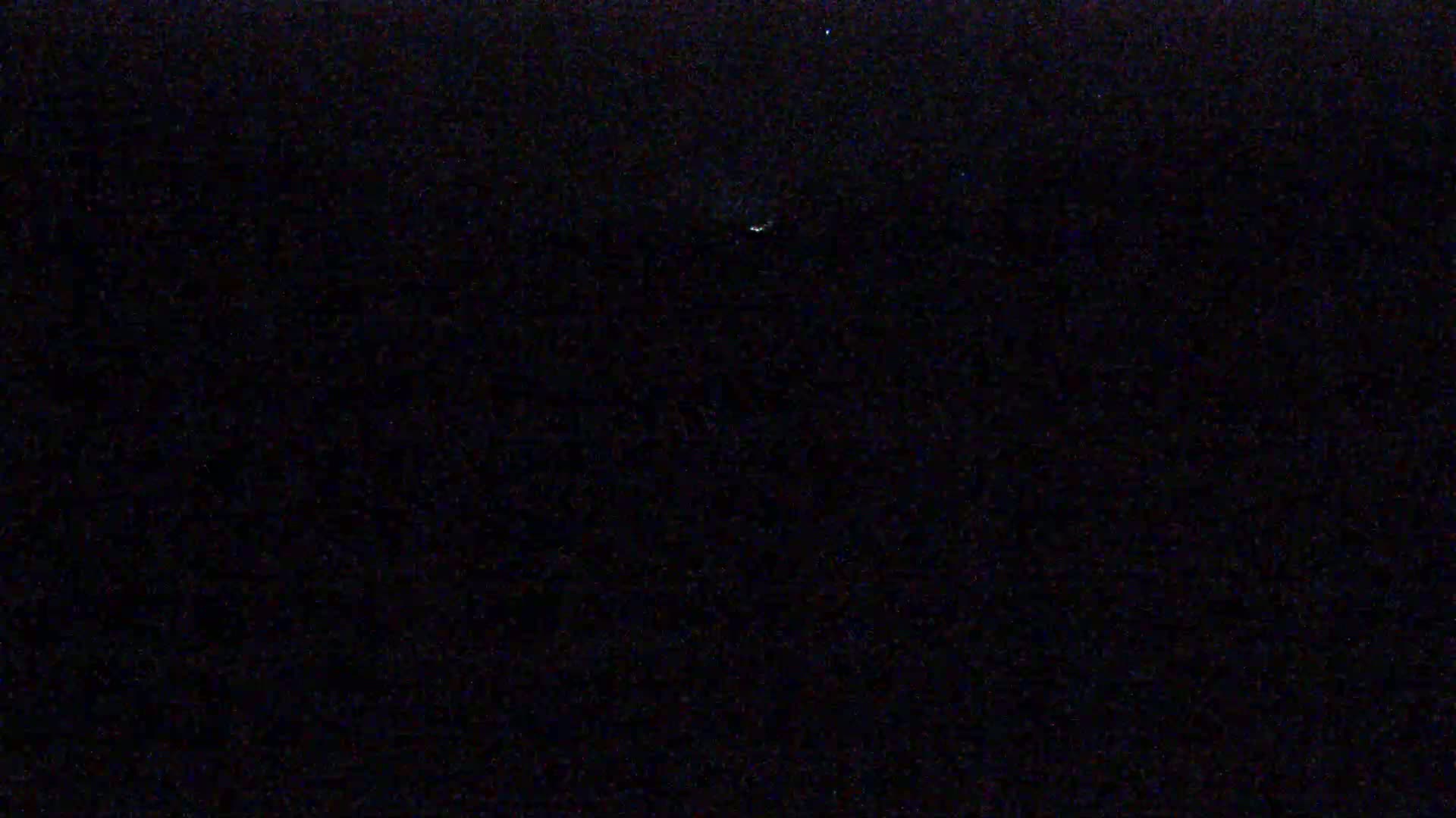 A dark, nighttime scene shows a faint, blurry light source in the center of the image.