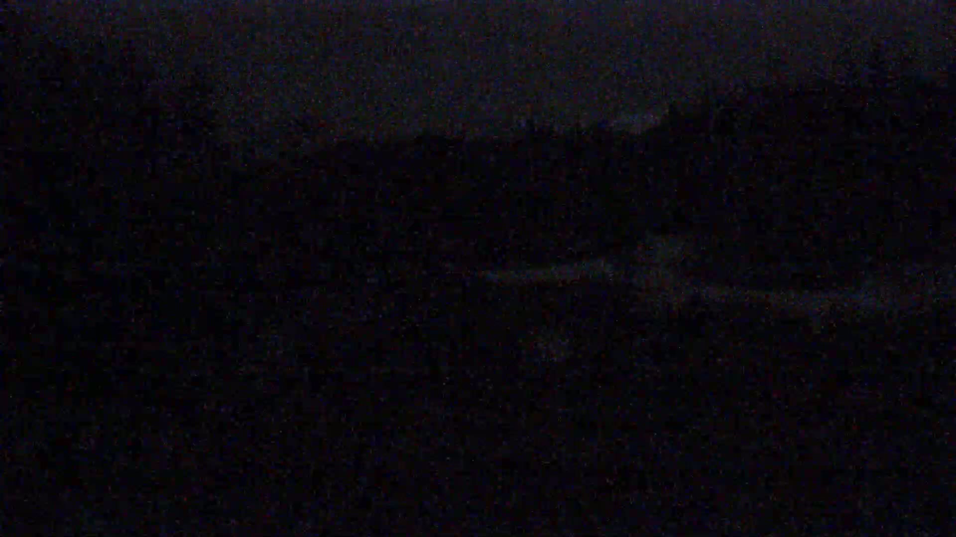 A dark, nighttime scene shows a dimly lit landscape with indistinct features under a dark sky.