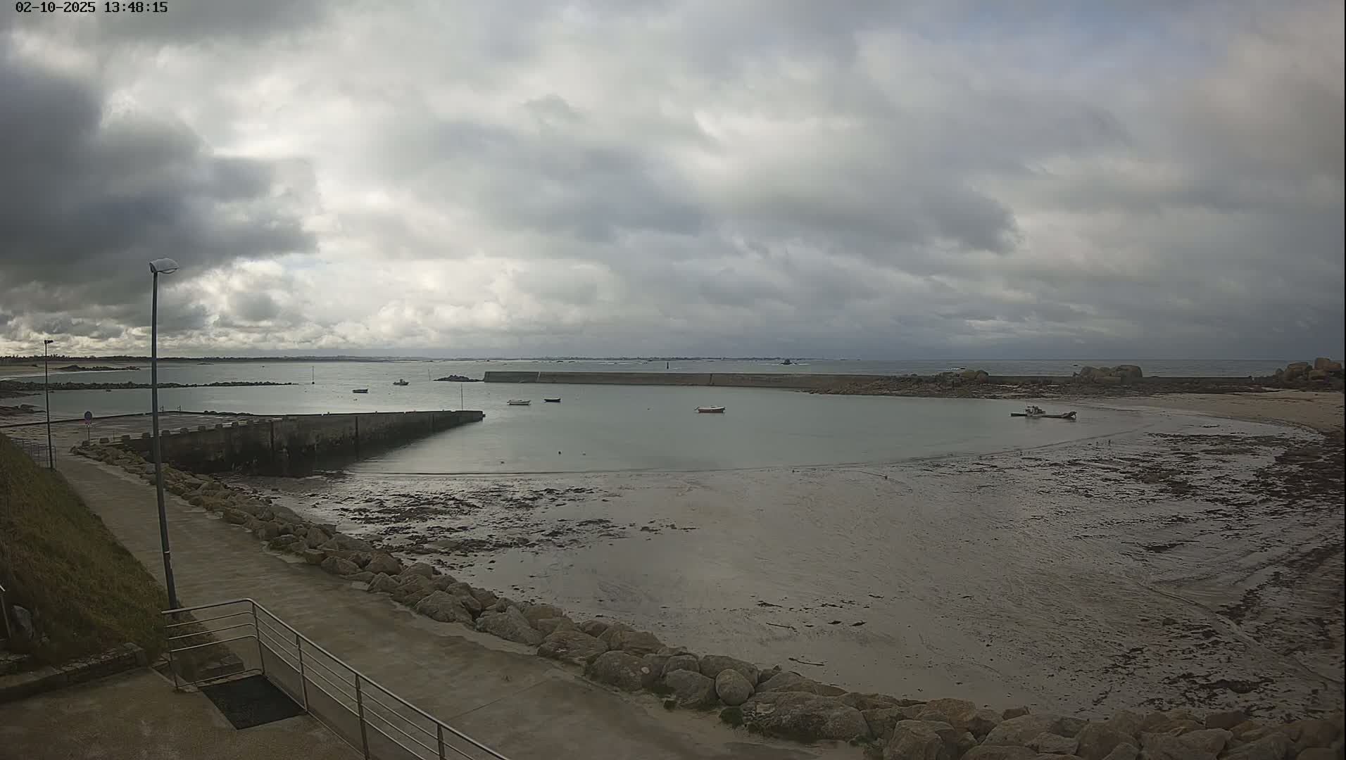 A small harbor with several boats is visible, under an overcast sky, with a low tide exposing a large expanse of mudflats.