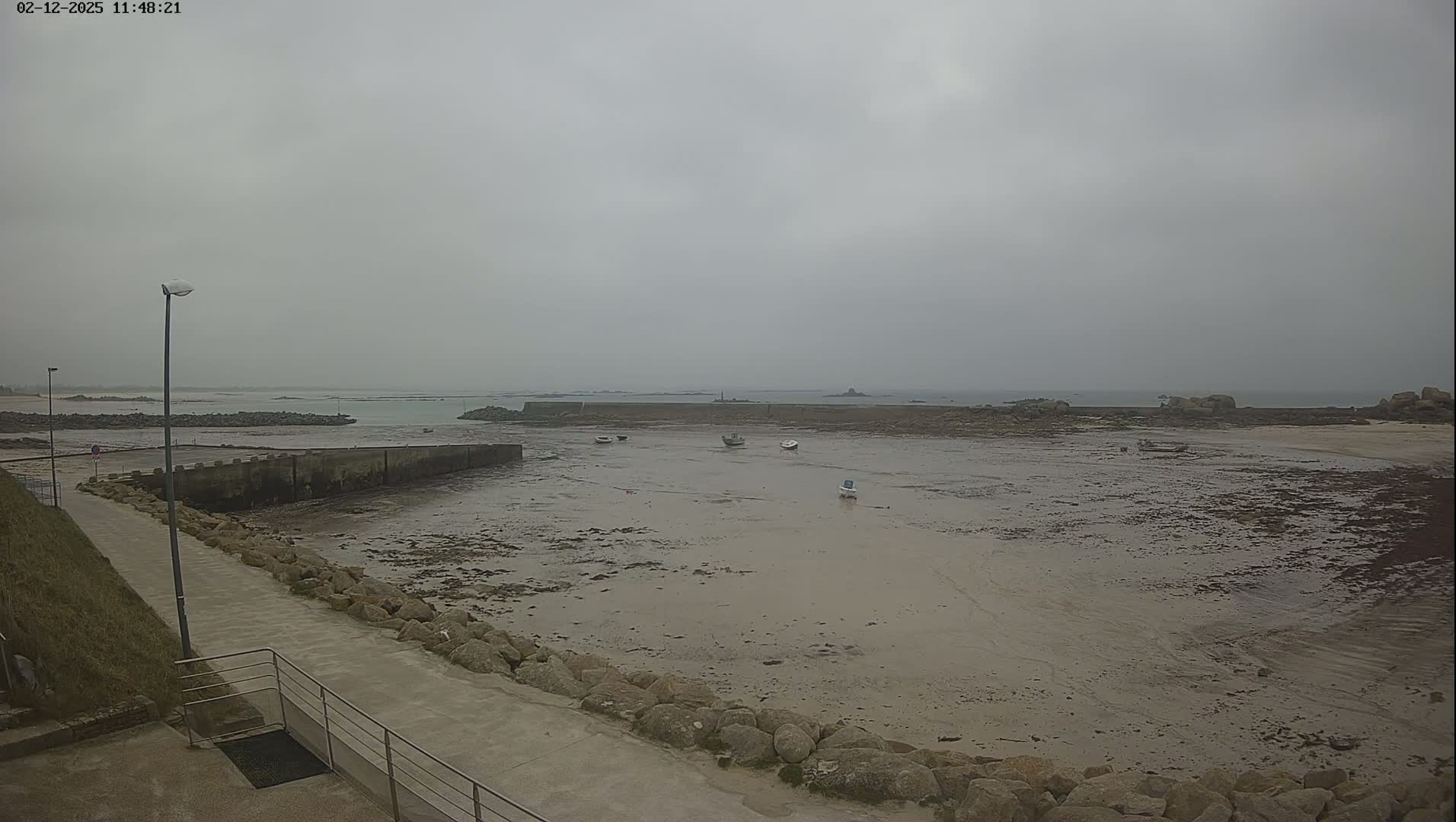 A low-tide, overcast day reveals a rocky shoreline with several small boats resting in a shallow harbor.