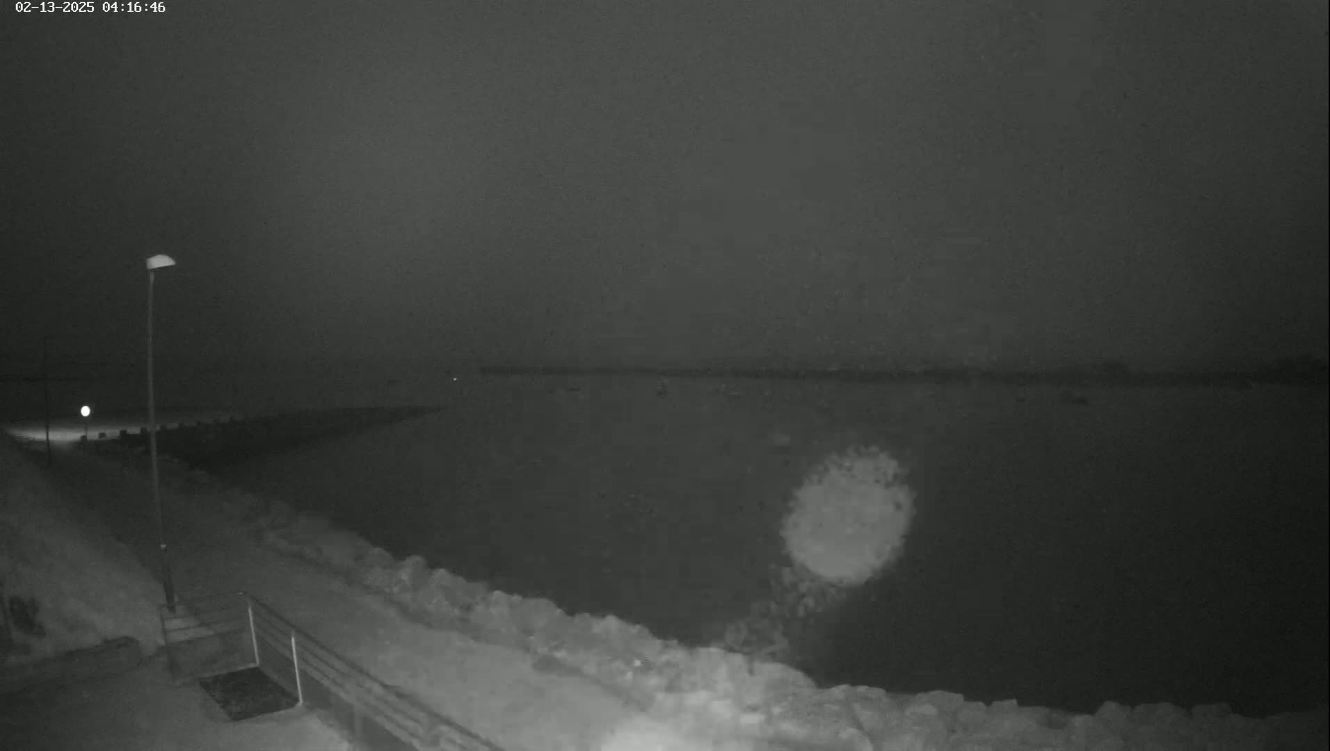 A snow-covered walkway next to a dark body of water under a nighttime sky.