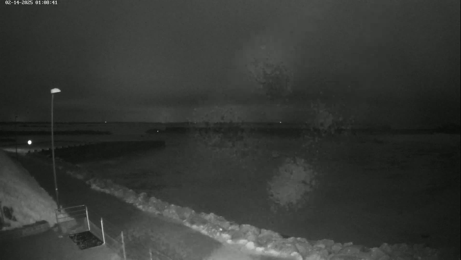 A nighttime, low-light view shows a rocky shoreline and choppy water under a dark sky.