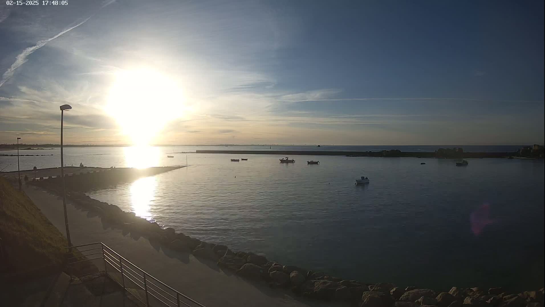 A calm harbor with several small boats is seen at sunset under a mostly clear sky.