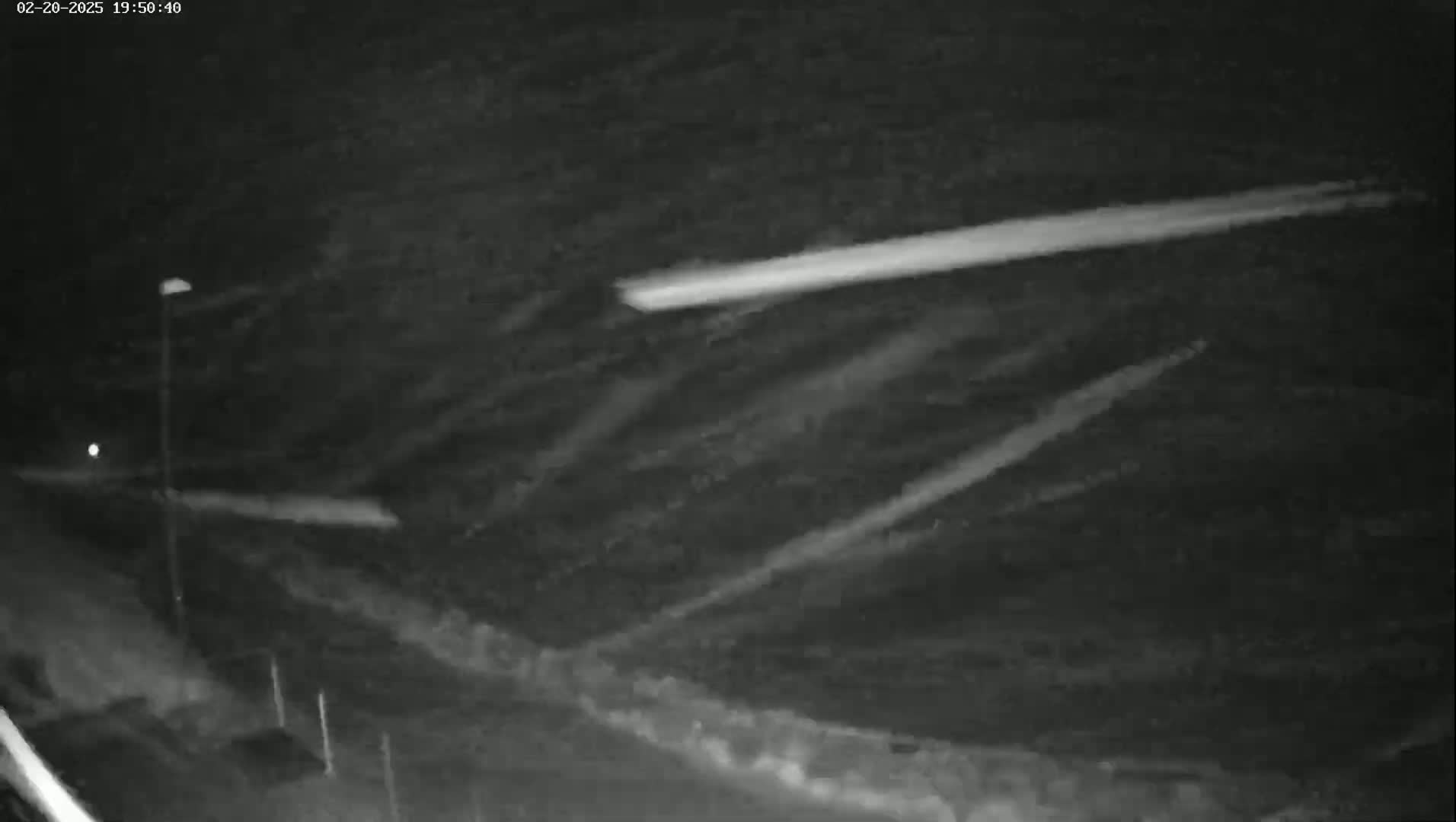 A nighttime, low-light view shows several bright streaks across a dark, possibly cloudy sky, with a streetlight visible in the lower left corner.
