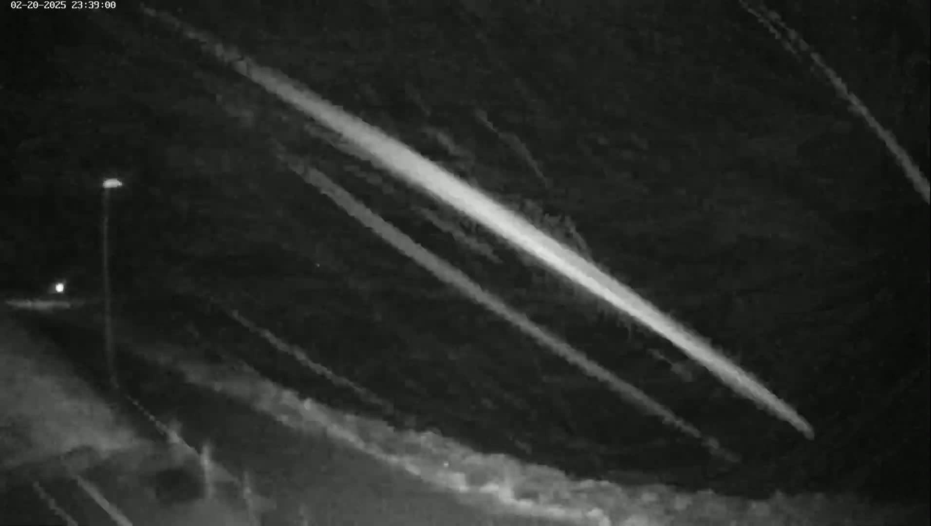 A nighttime scene shows several bright streaks of light across a dark sky near a lone streetlight.