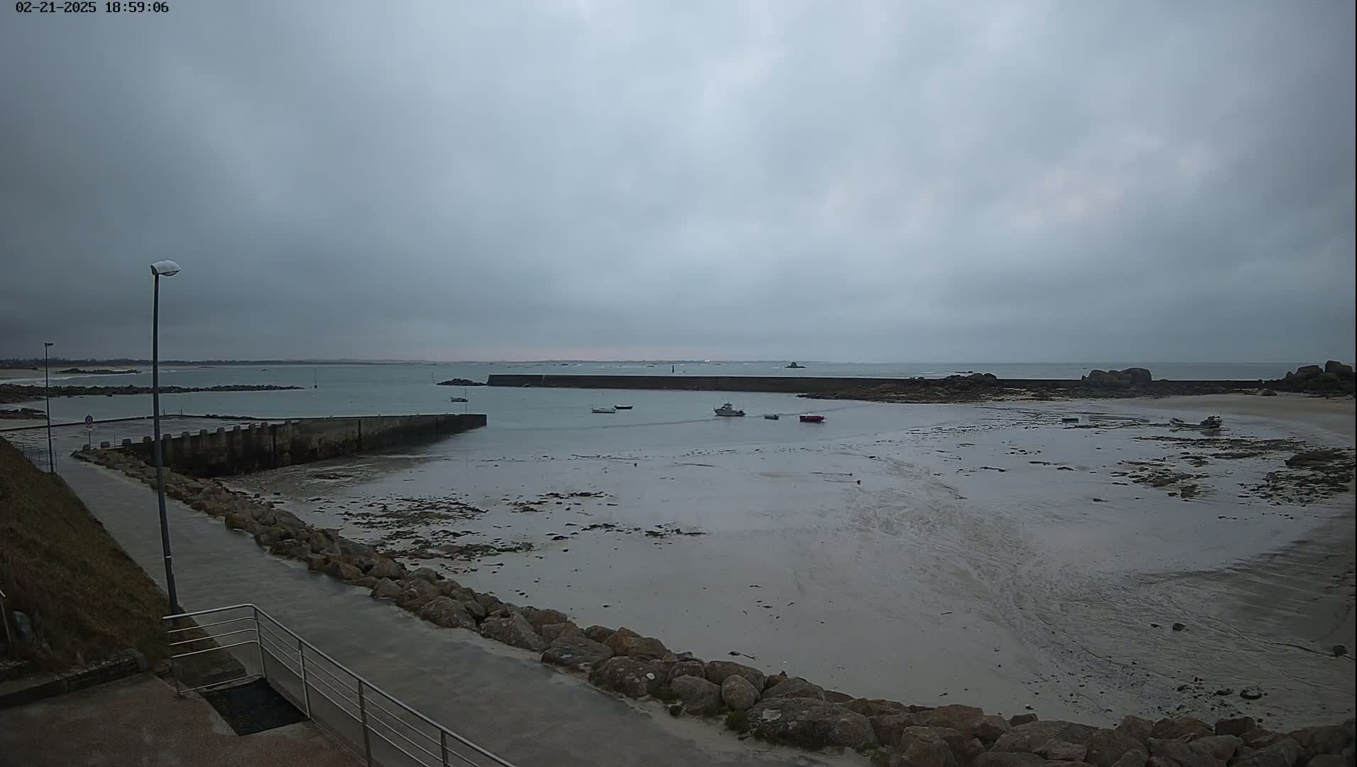 A small harbor with several boats sits at low tide under an overcast sky.