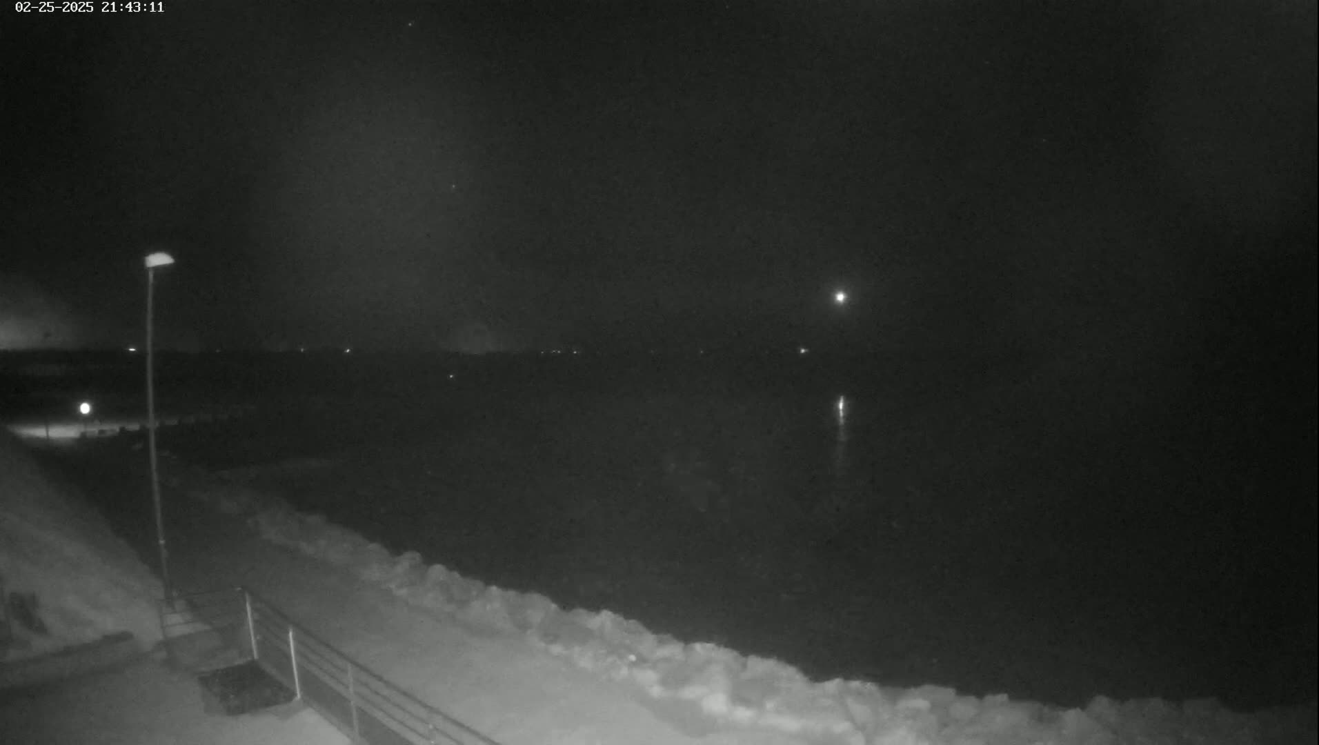 A nighttime view of a snow-covered shoreline and dark water under a mostly clear sky.