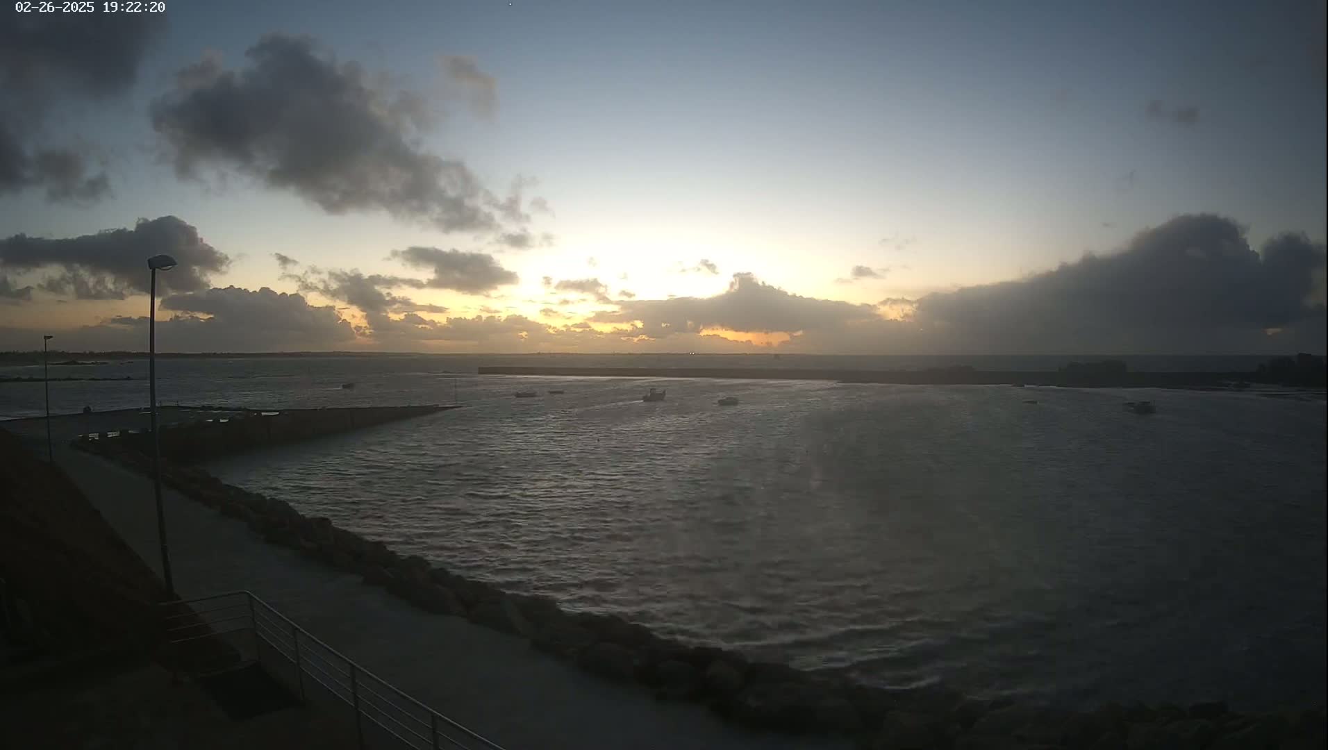 A partly cloudy sunset over a choppy harbor with several small boats.