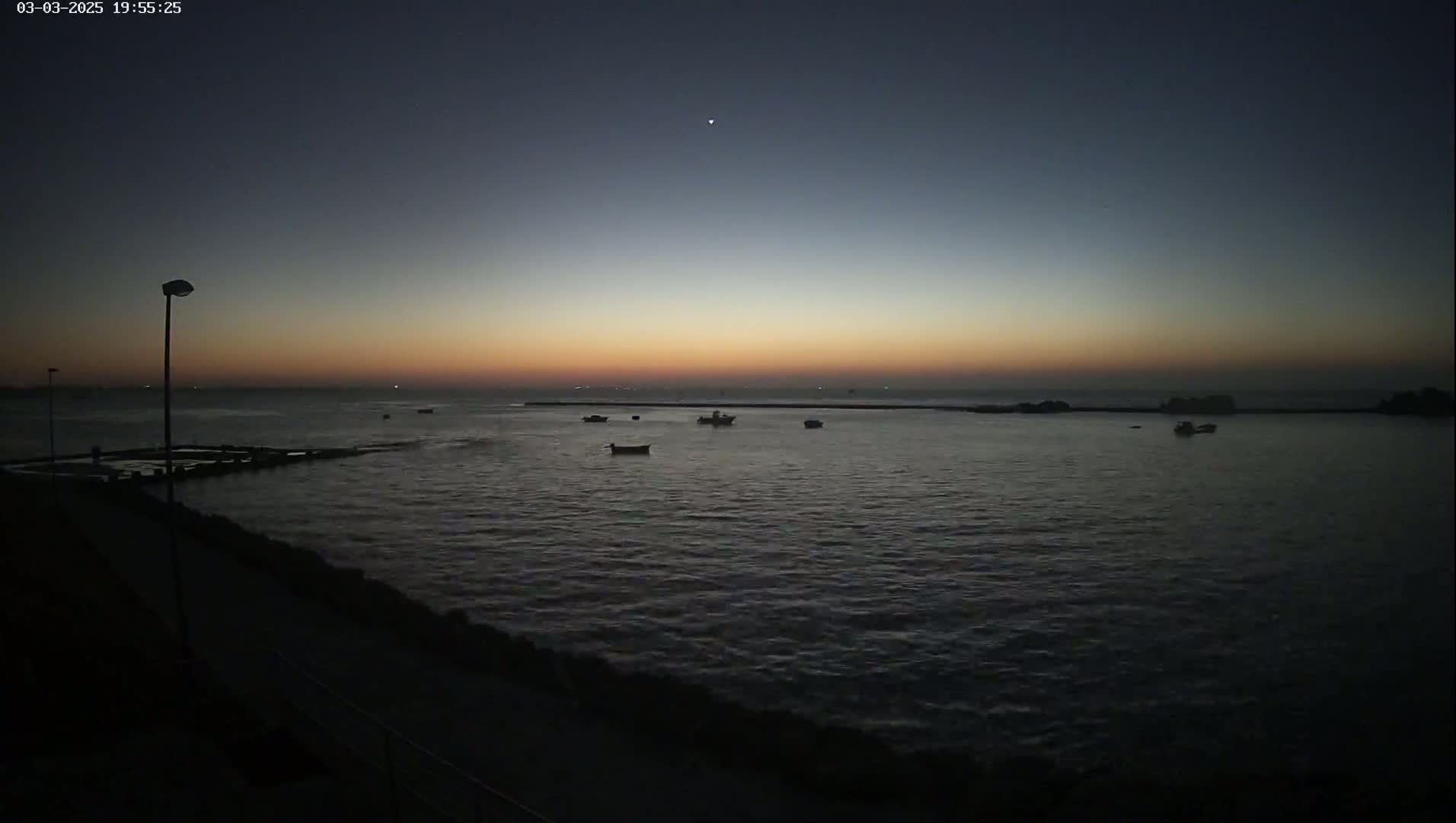 Several small boats are visible on a dark body of water at sunset under a mostly clear sky.