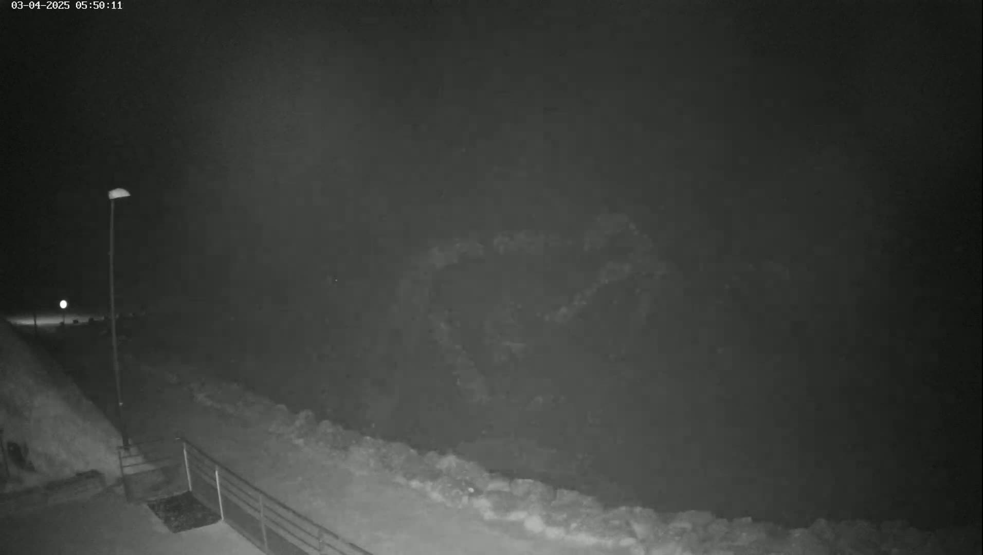 A nighttime, low-light view shows a snow-covered path and embankment under a dark, cloudy sky.