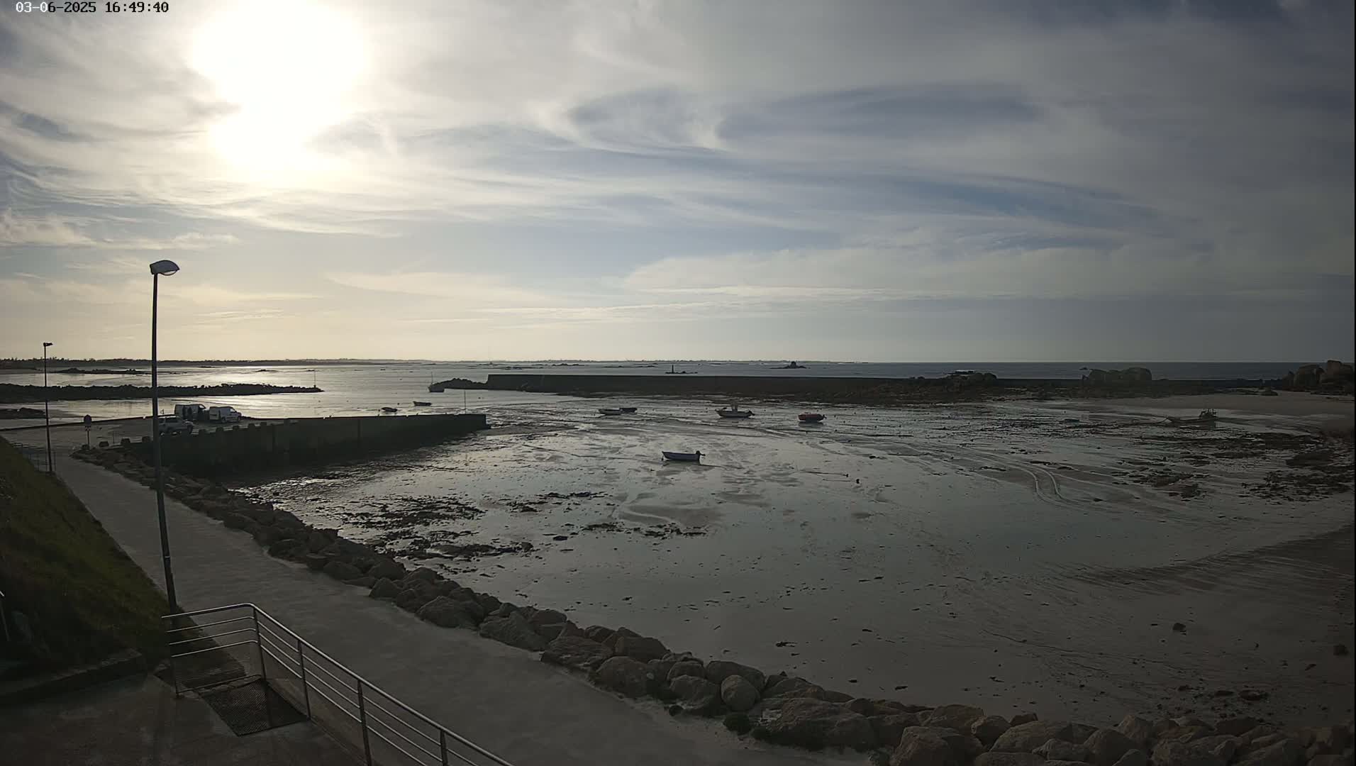 A mostly cloudy day reveals a rocky shoreline with several small boats in a shallow, exposed harbor.