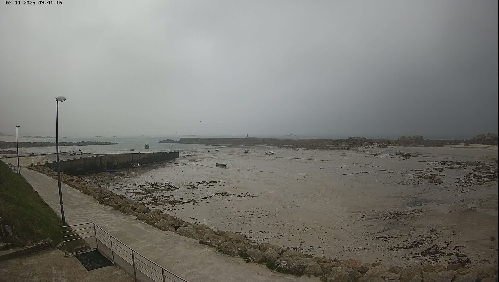 A low-lying, mostly exposed harbor with several small boats sits under a gray, overcast sky.