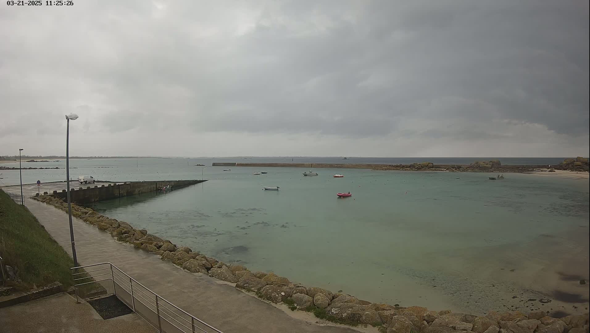 A calm, shallow, green-tinged bay with several small boats is seen under an overcast sky.