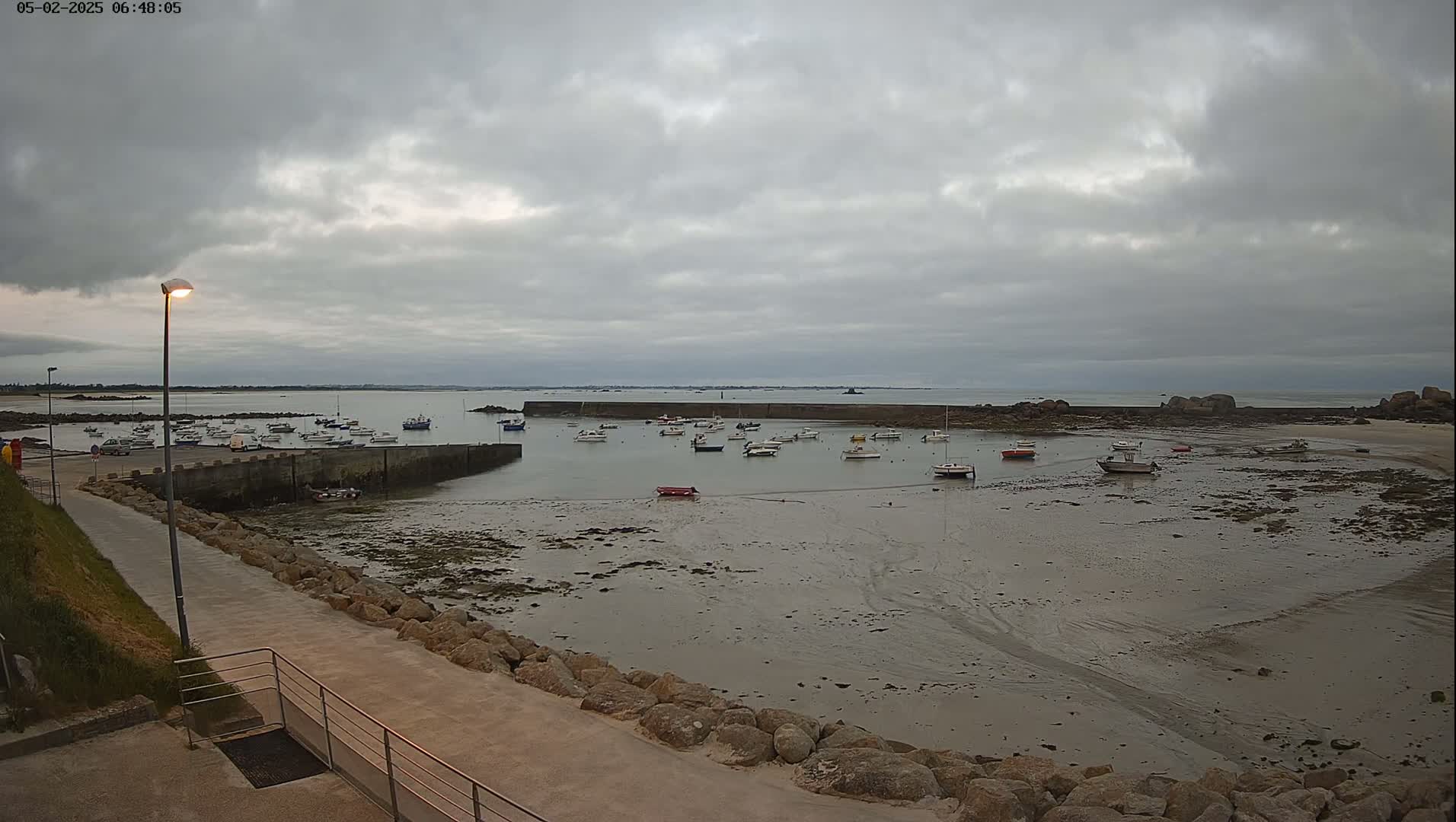 A harbor with numerous small boats sits partially exposed at low tide under a cloudy sky.