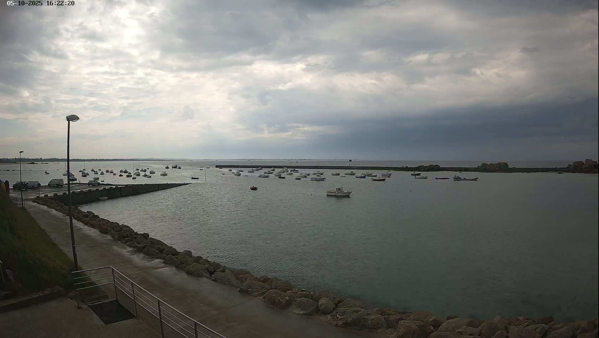 Many small boats are moored in a calm harbor under a cloudy sky.