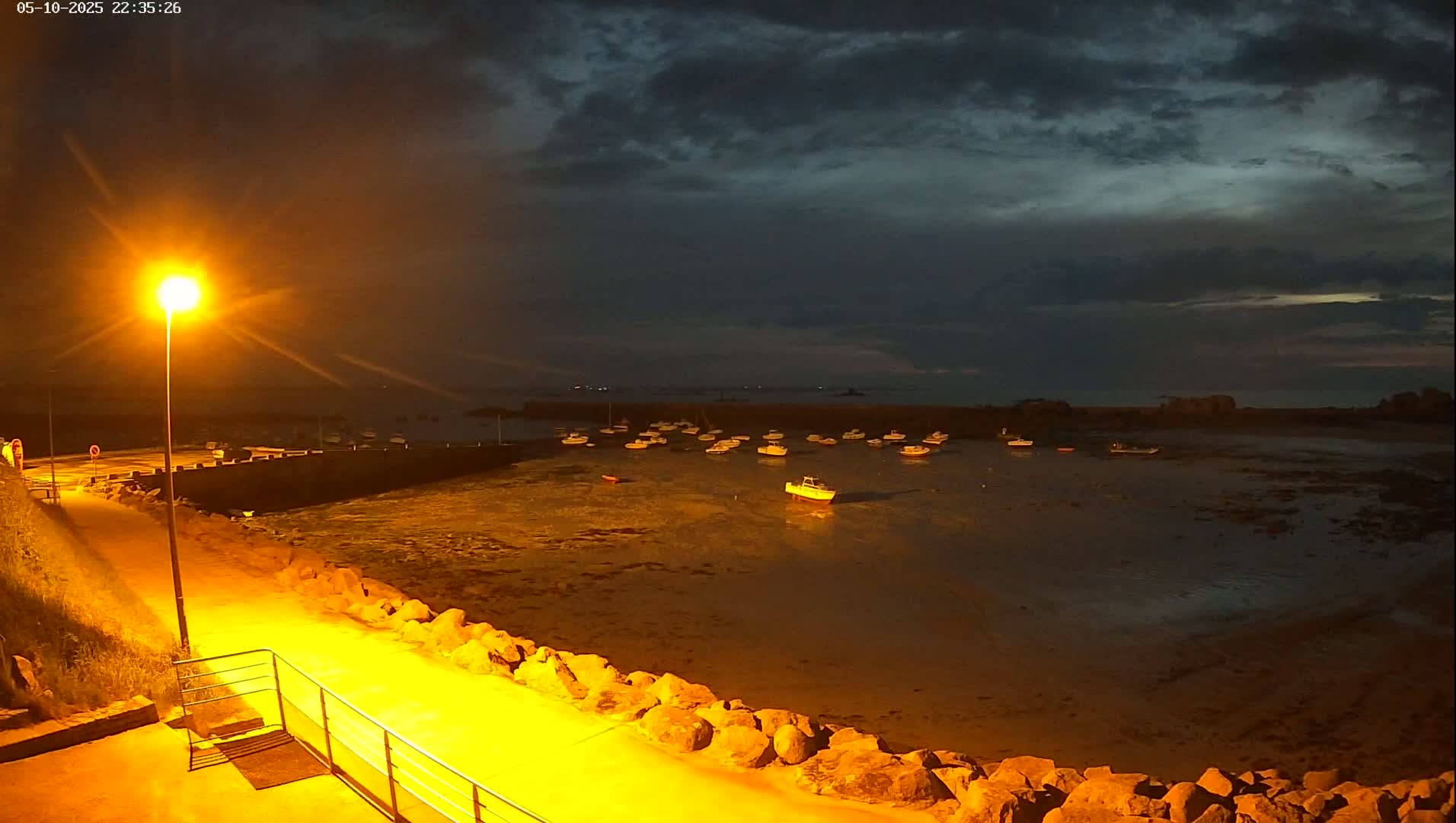 A nighttime view of a harbor filled with boats under a dark, cloudy sky illuminated by a single lamppost.