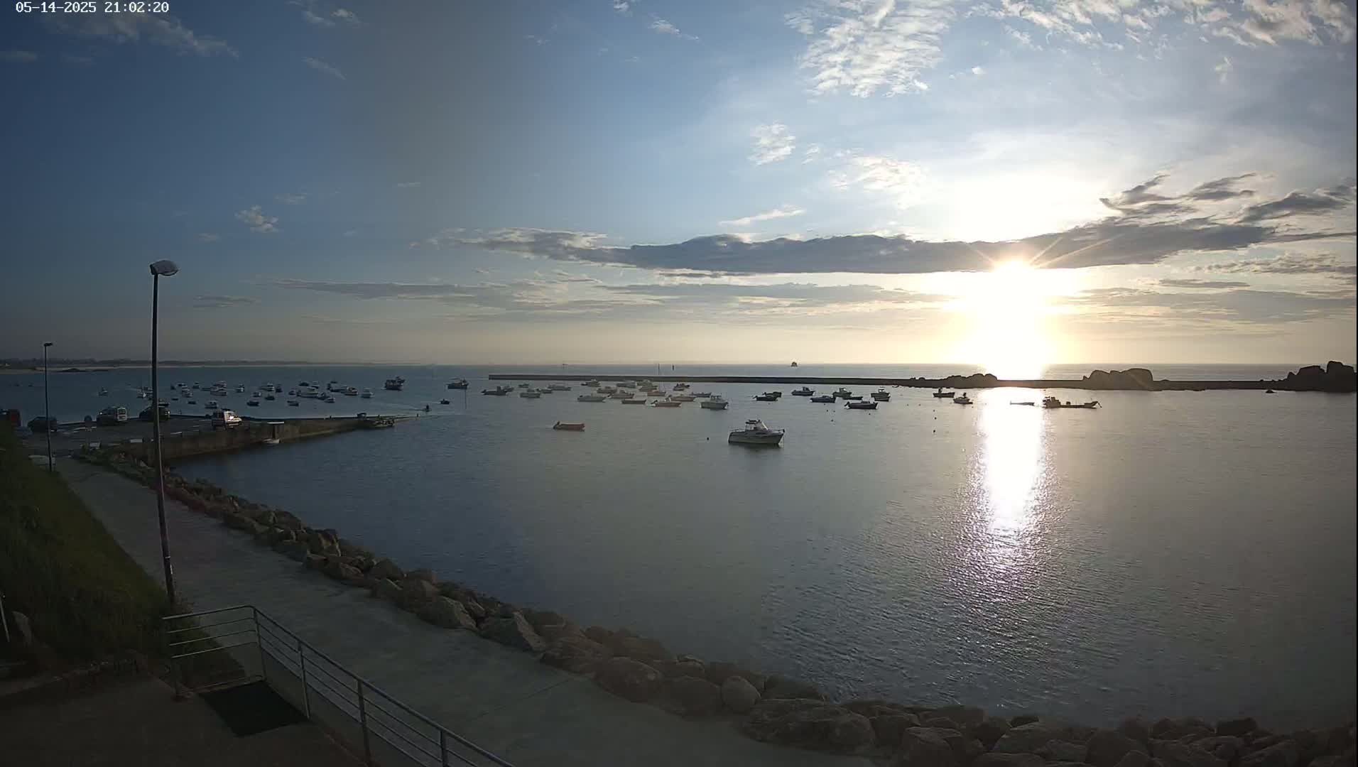 Many small boats are moored in a calm harbor at sunset under a partly cloudy sky.
