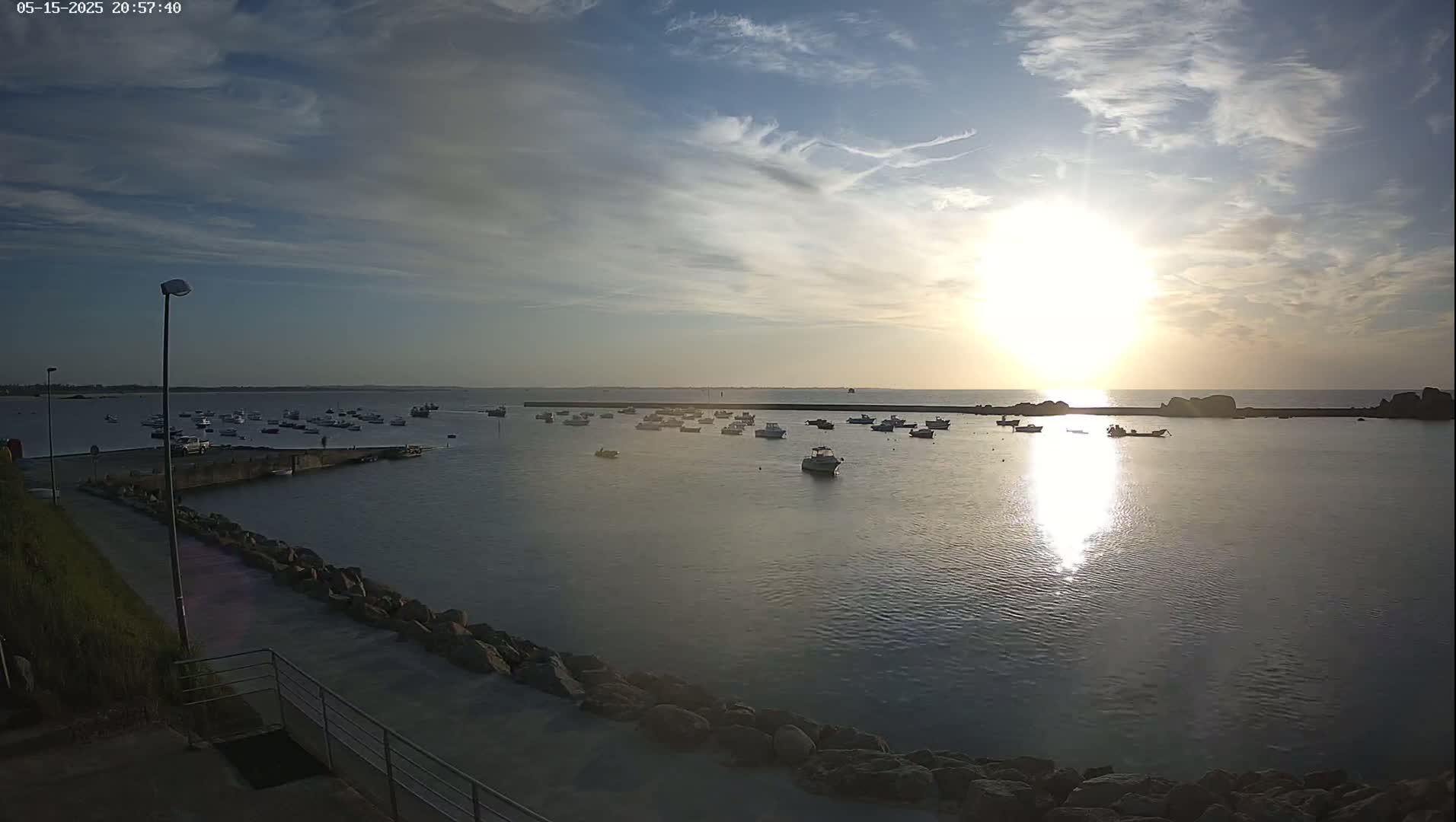 Numerous small boats are moored in a calm harbor at sunset under a partly cloudy sky.