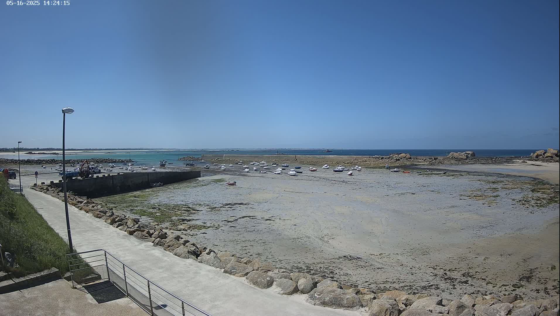 A harbor with numerous small boats rests on a mostly exposed sandy seabed under a clear blue sky.