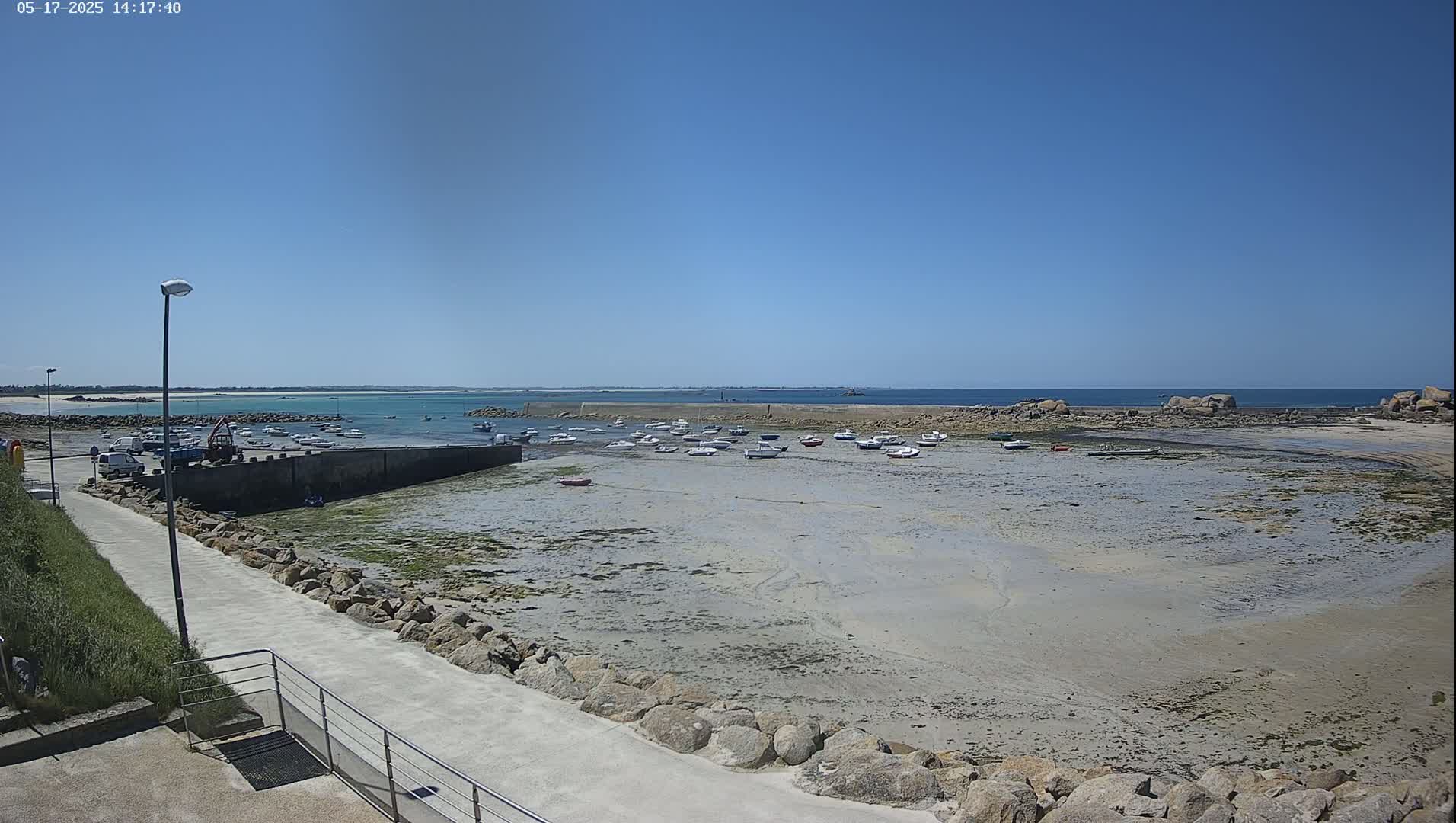 A small harbor with numerous boats resting on exposed sand at low tide under a clear, sunny sky.