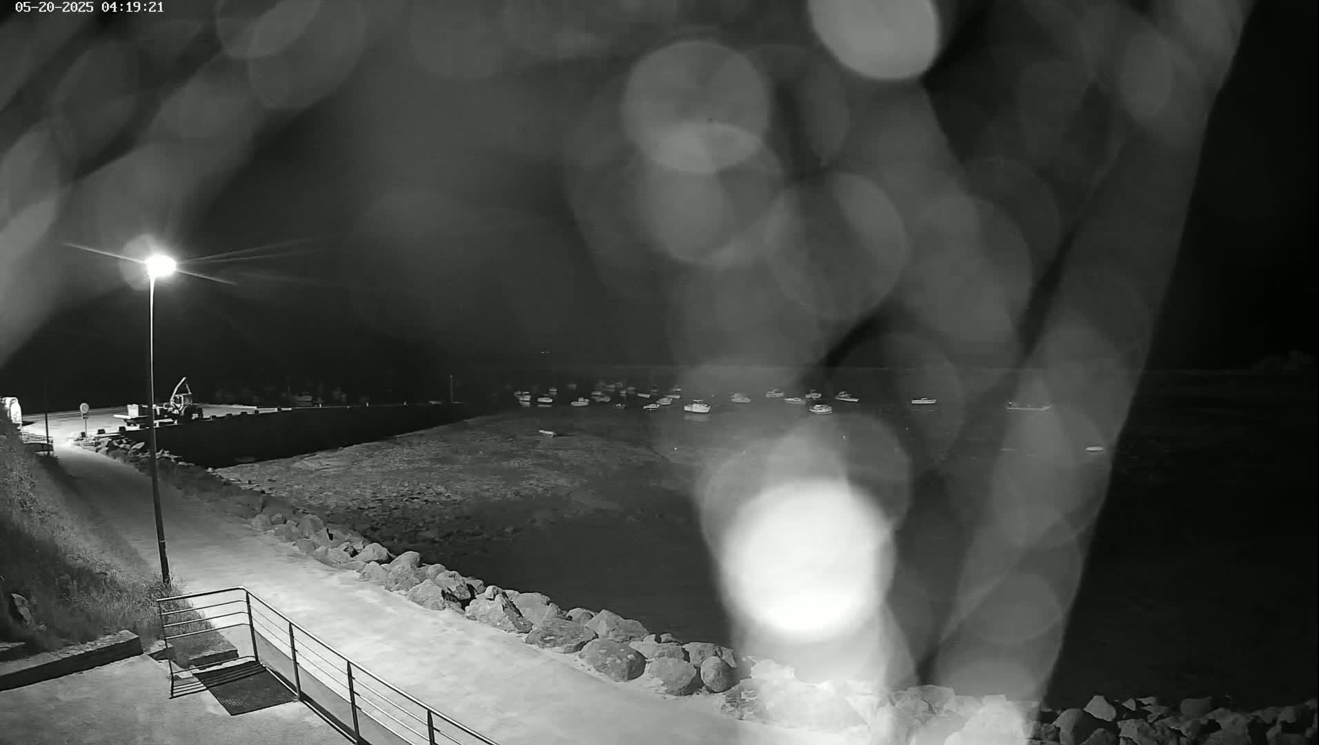 A nighttime view of a harbor filled with boats, seen through rain-covered glass, with a lit pathway leading to the water's edge.