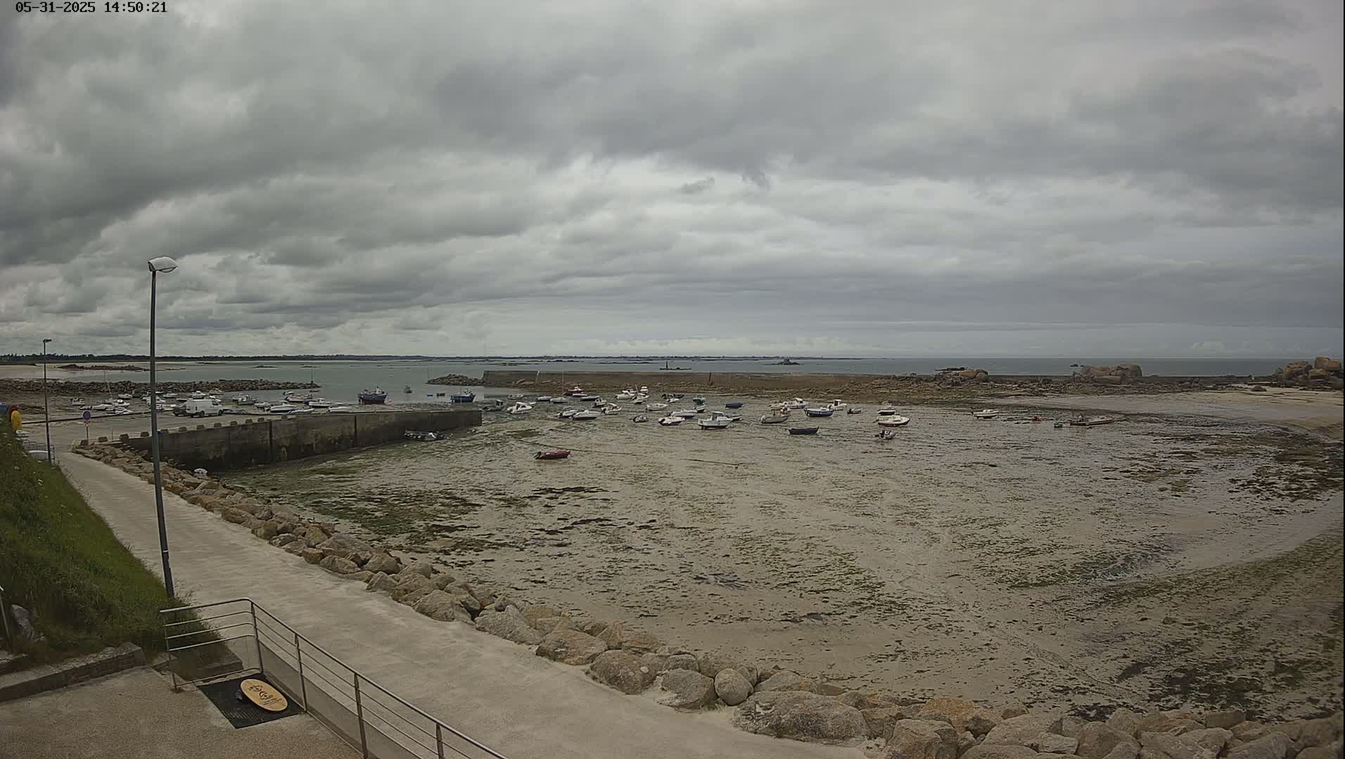 A small harbor with numerous boats sits exposed at low tide under a cloudy sky.