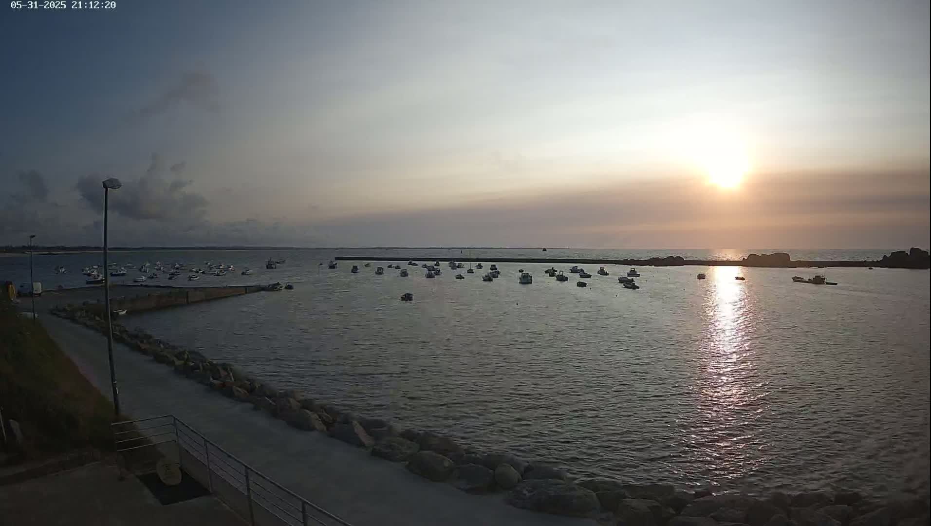 Many small boats are moored in a calm harbor at sunset under a partly cloudy sky.
