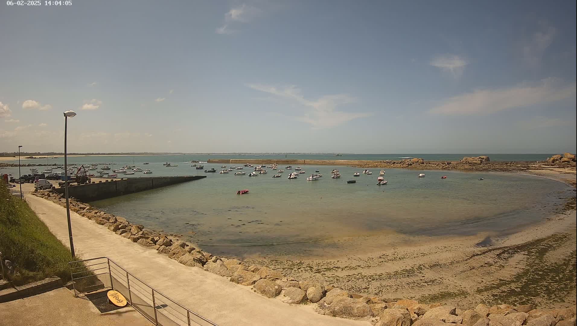 A calm, sunny day reveals a small harbor filled with numerous boats, nestled within a rocky cove that opens to a tranquil sea.