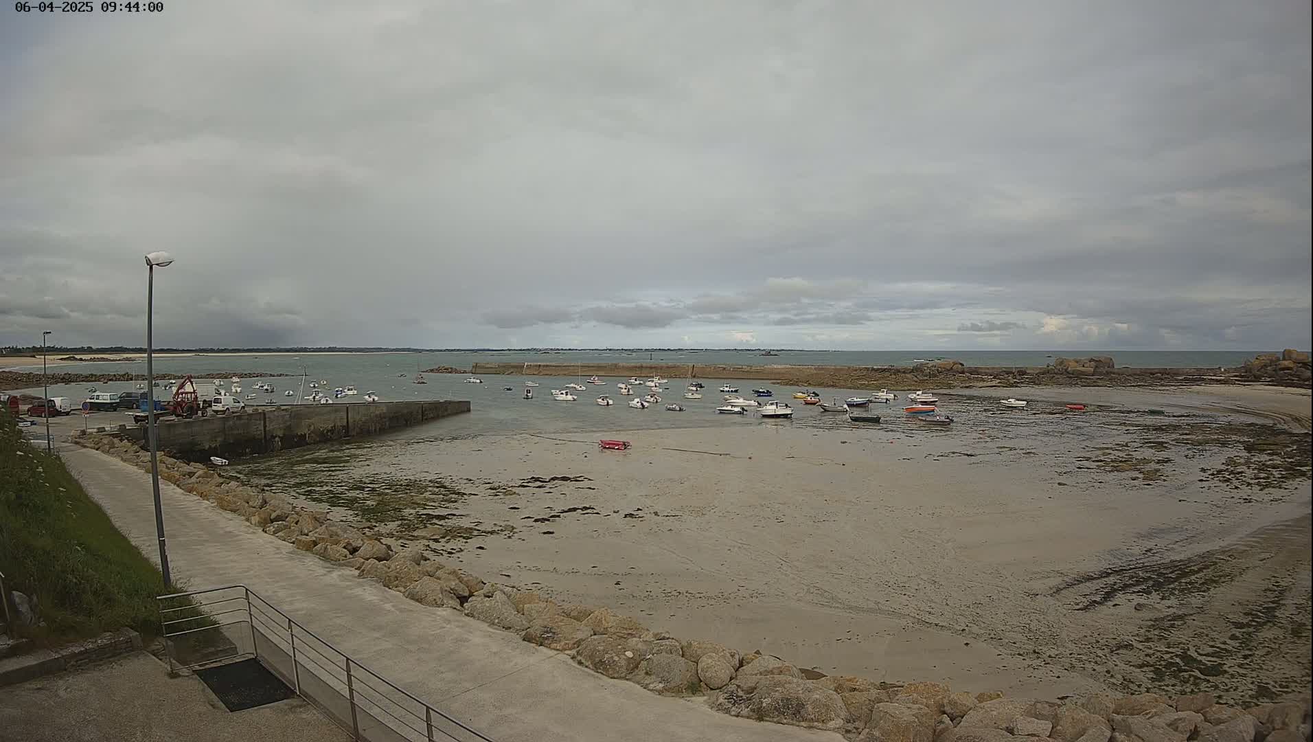 A small harbor with numerous boats sits on a sandy shore under an overcast sky.