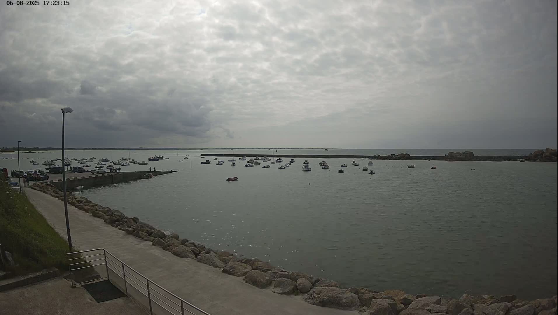 Many small boats are moored in a calm harbor under an overcast sky.