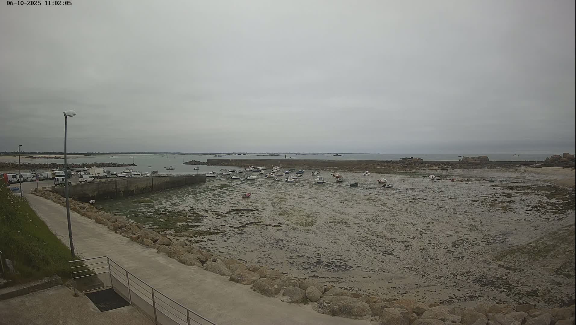 A small harbor with numerous boats sits partially exposed at low tide under an overcast sky.
