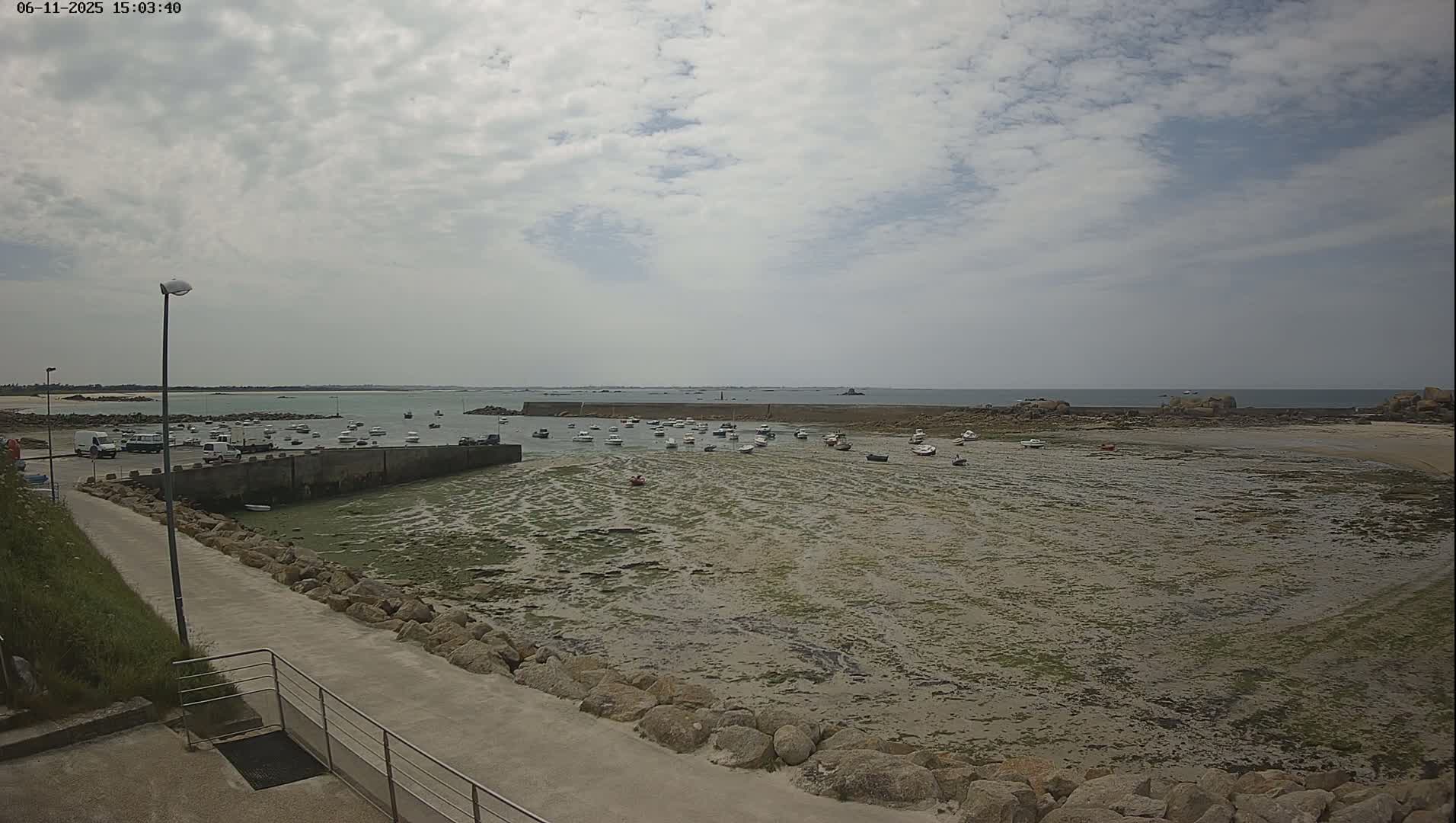 A small harbor with numerous boats rests at low tide under a partly cloudy sky.