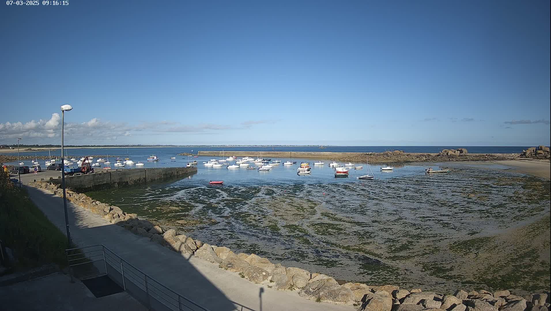 A small harbor filled with numerous boats is nestled in a rocky cove, under a clear blue sky.