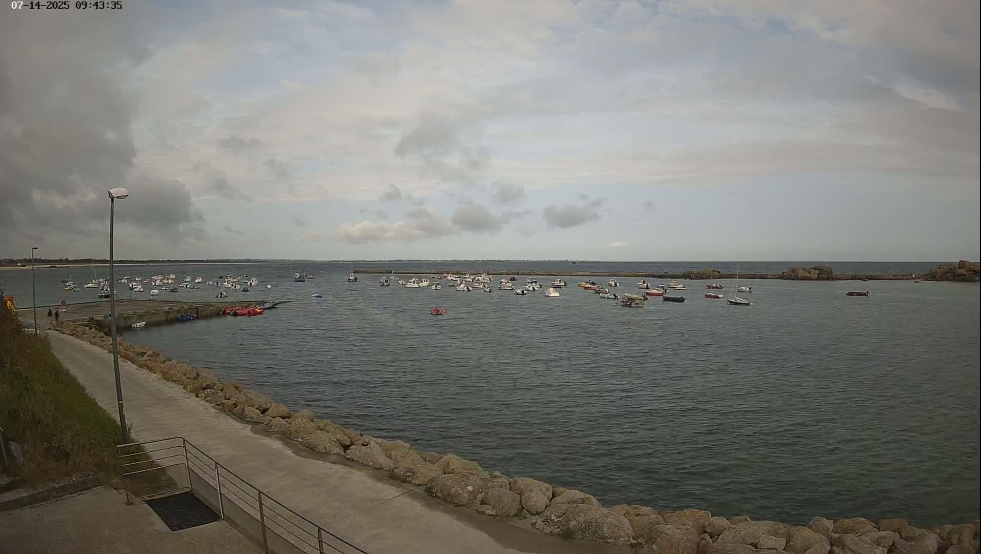 A calm harbor filled with numerous small boats under a mostly cloudy sky.