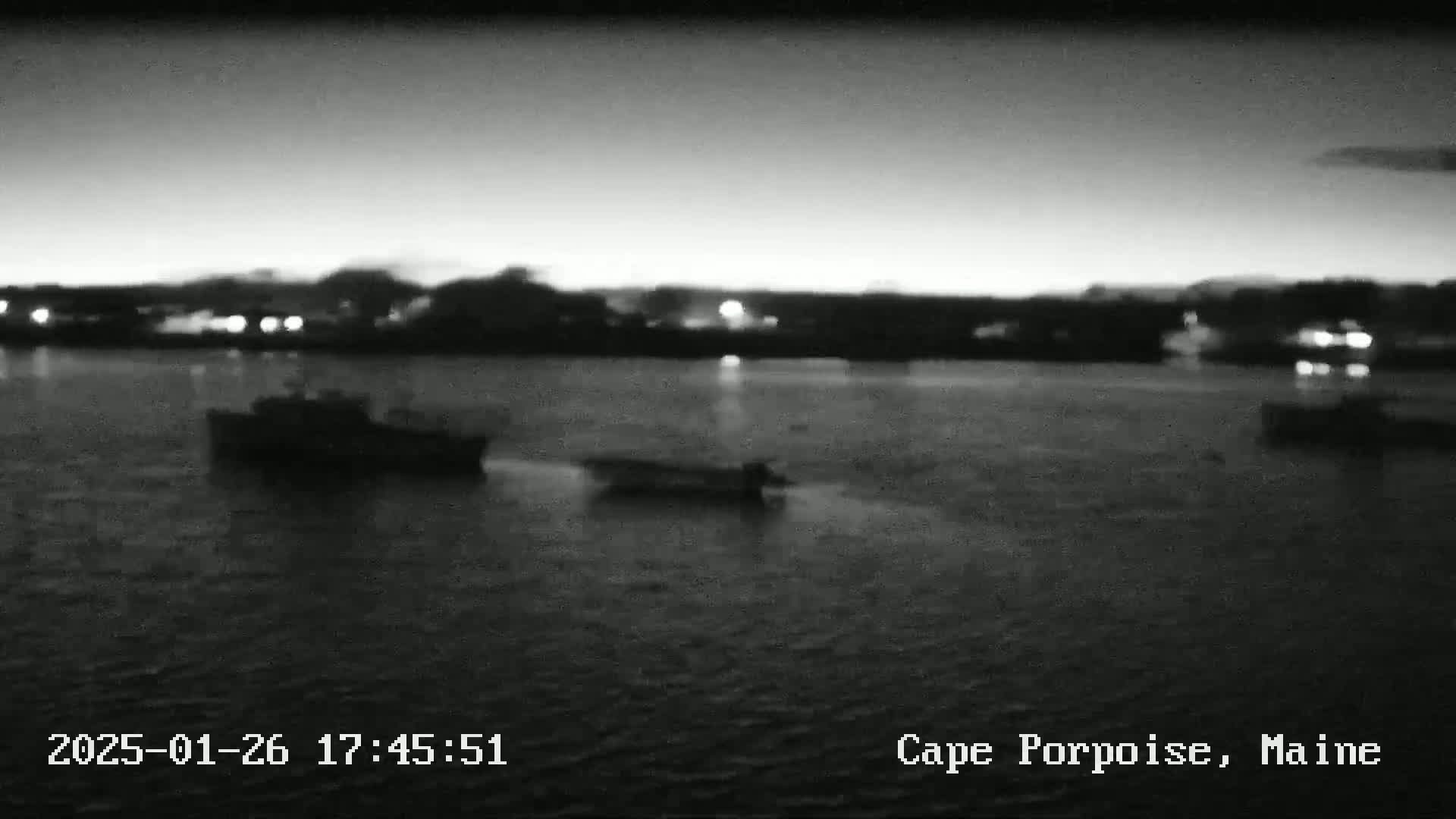 At dusk, several small boats are visible on calm water in front of a dimly lit shoreline.