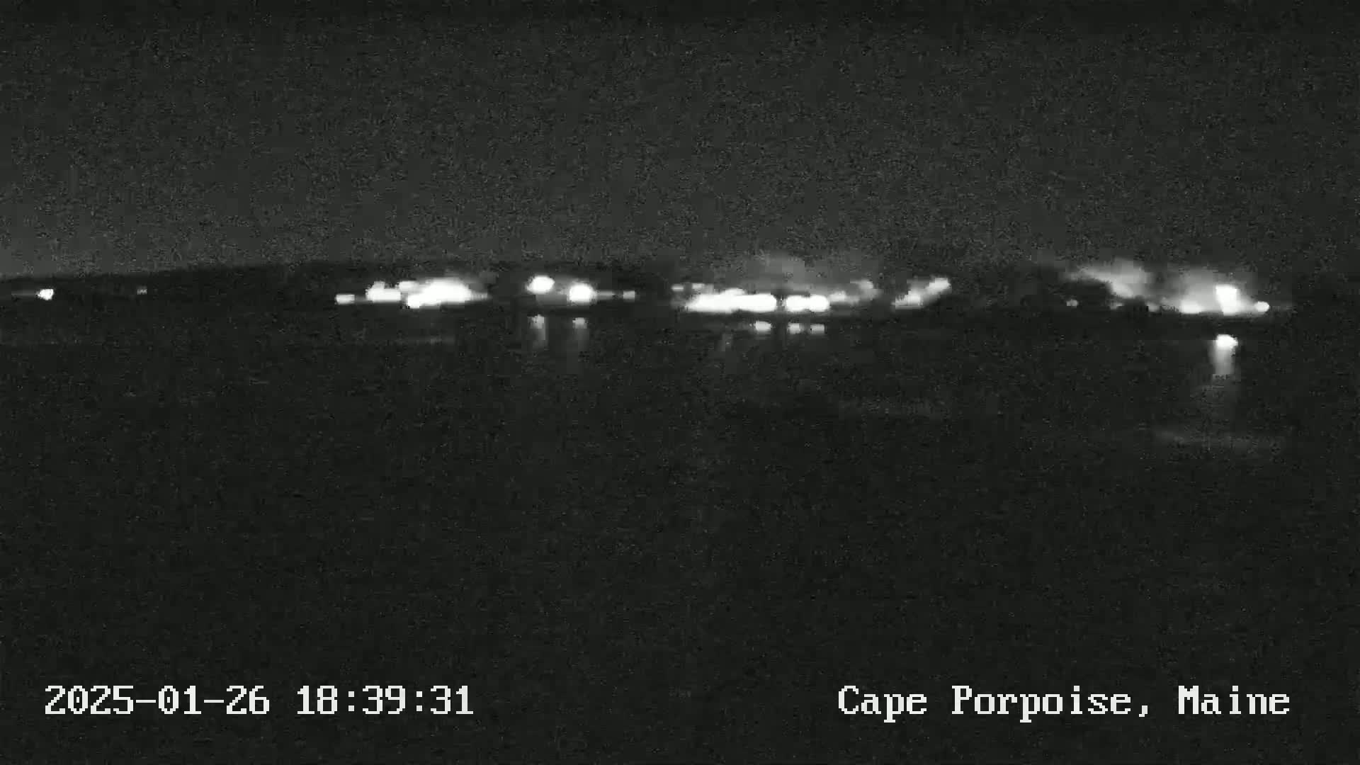 At night, a blurry, low-light image shows a line of distant lights across a dark body of water.
