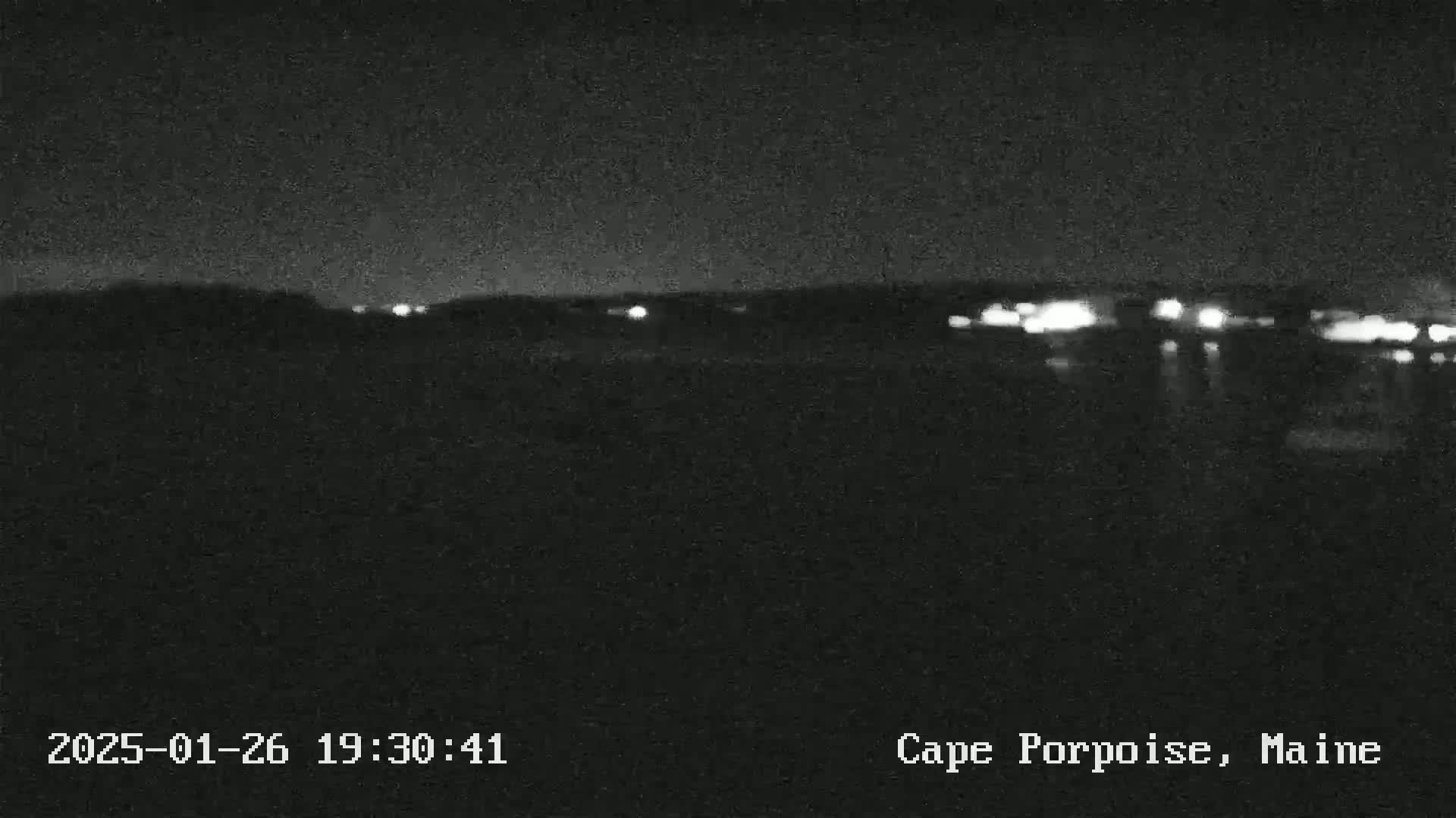 Here is a description of the image: A nighttime view shows a dark landscape with a line of distant lights across the horizon.