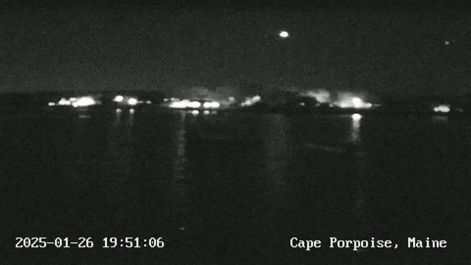 A nighttime view of a body of water with lights from a town or city visible in the distance under a clear sky.