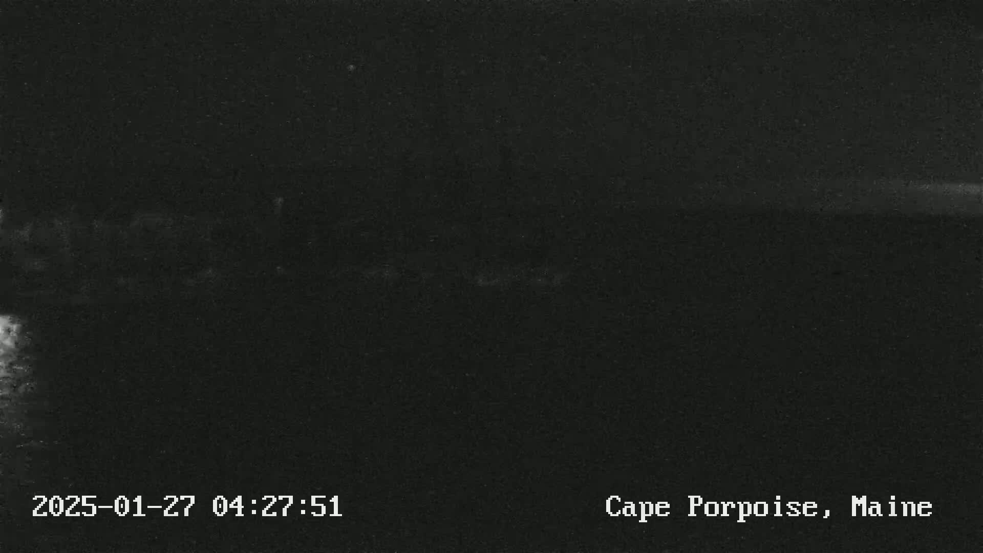 The image shows a very dark, nighttime scene, likely outdoors, with a faint, bright horizontal line near the top suggesting a distant horizon.
