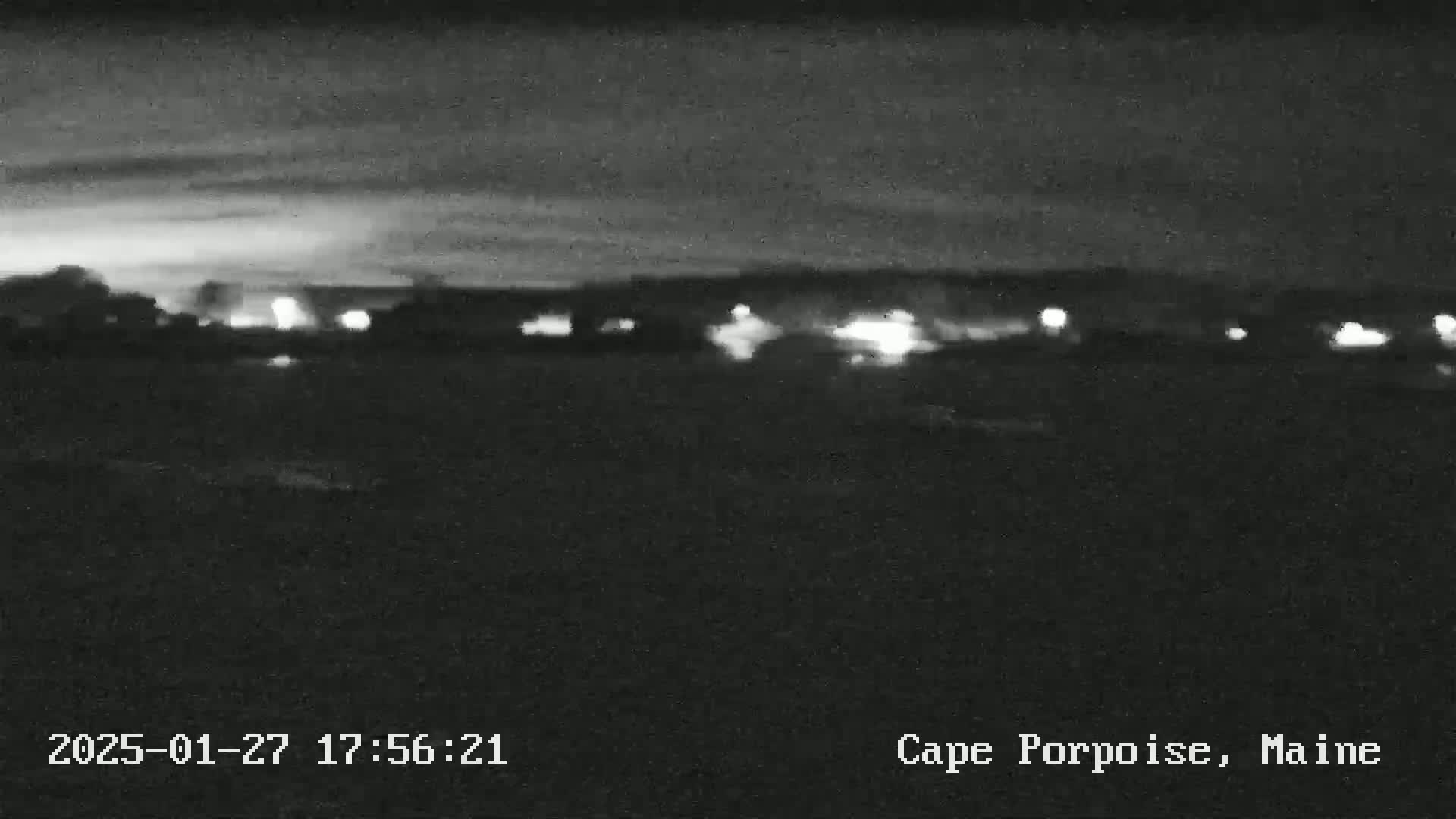 A nighttime, low-light view of a distant town or village with faint lights under a dark, cloudy sky.