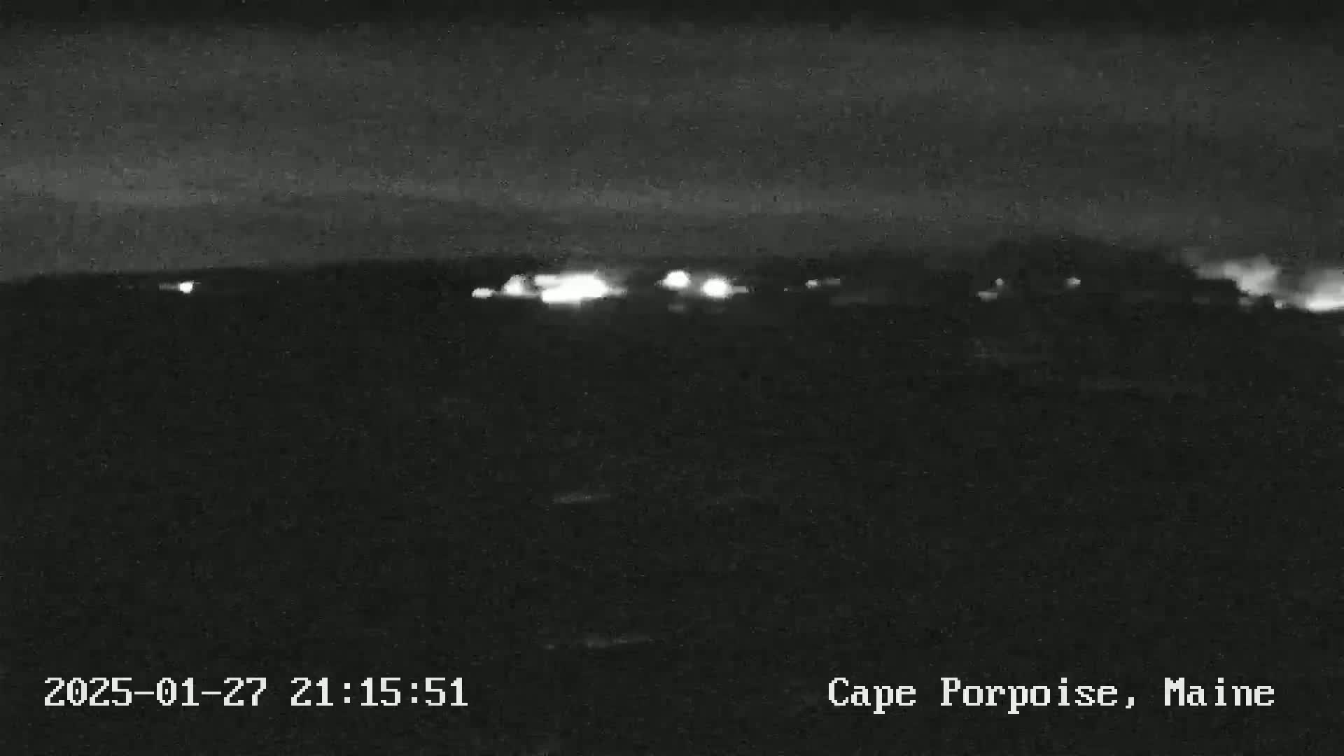 A nighttime, low-light view shows a distant line of lights, likely from a town or buildings, under a dark sky.