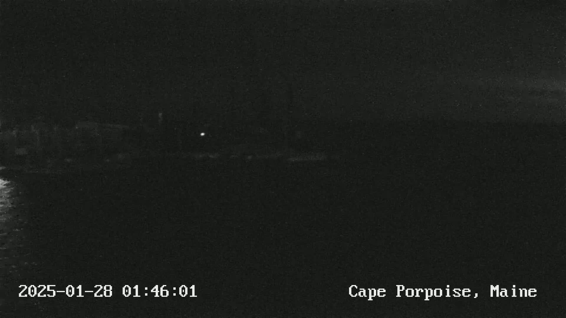 A dark, nighttime image shows a body of water with a barely visible shoreline in the distance under a clear, dark sky.