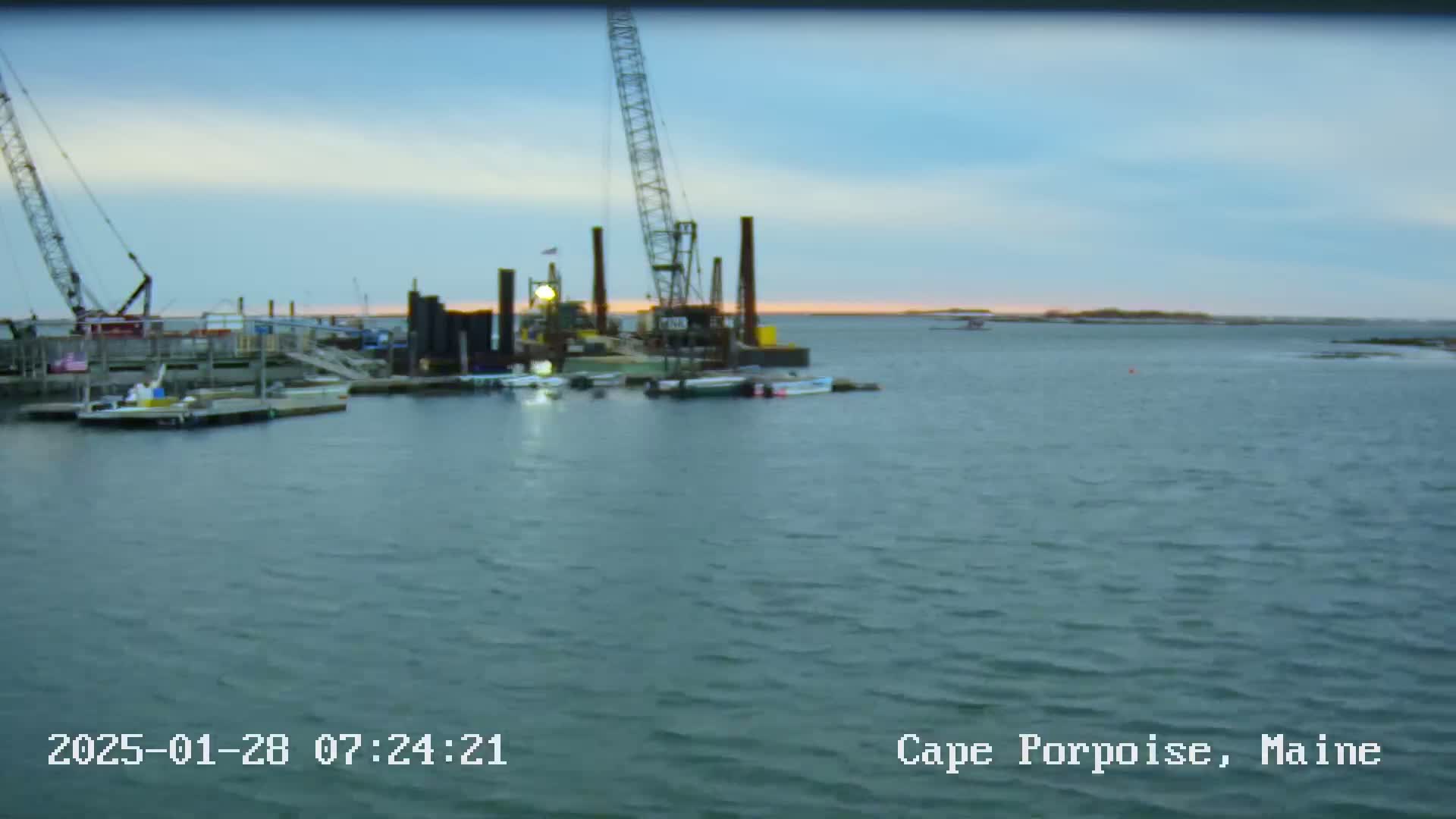 Construction equipment sits on a calm body of water at sunrise.