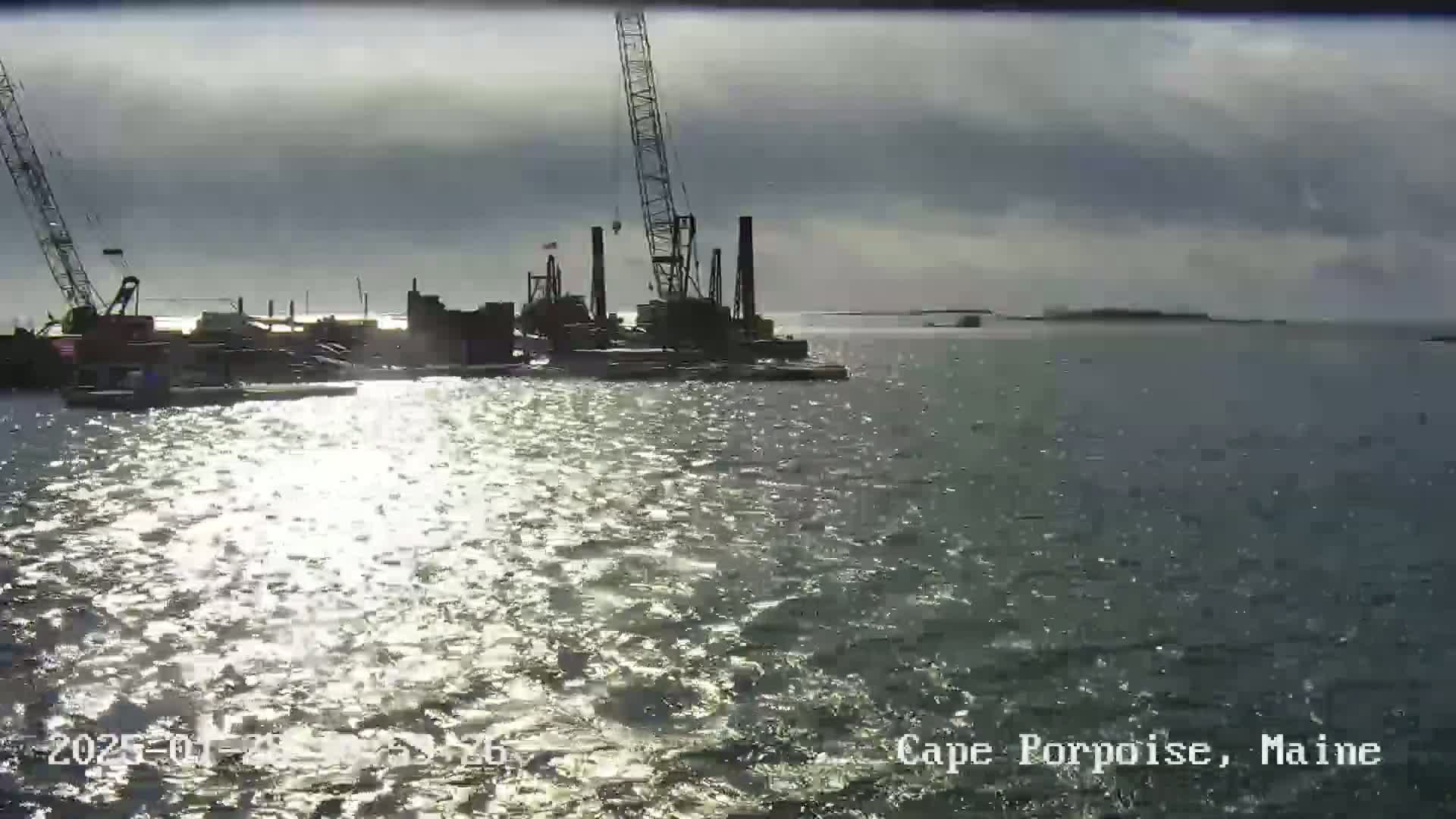Construction equipment sits on barges in a body of water under a partly cloudy sky.